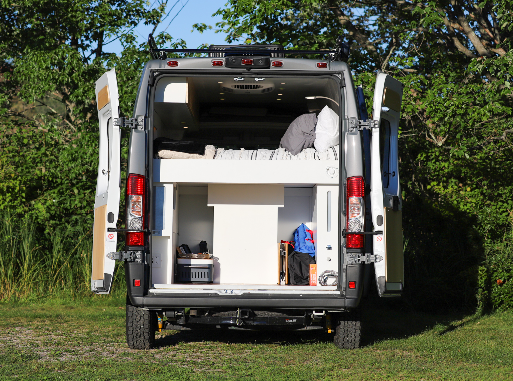 Back of a grey **rv rental** conversion van open, revealing a bed & gear storage, perfect for travel adventures.. Dodge Promaster 2500 2019