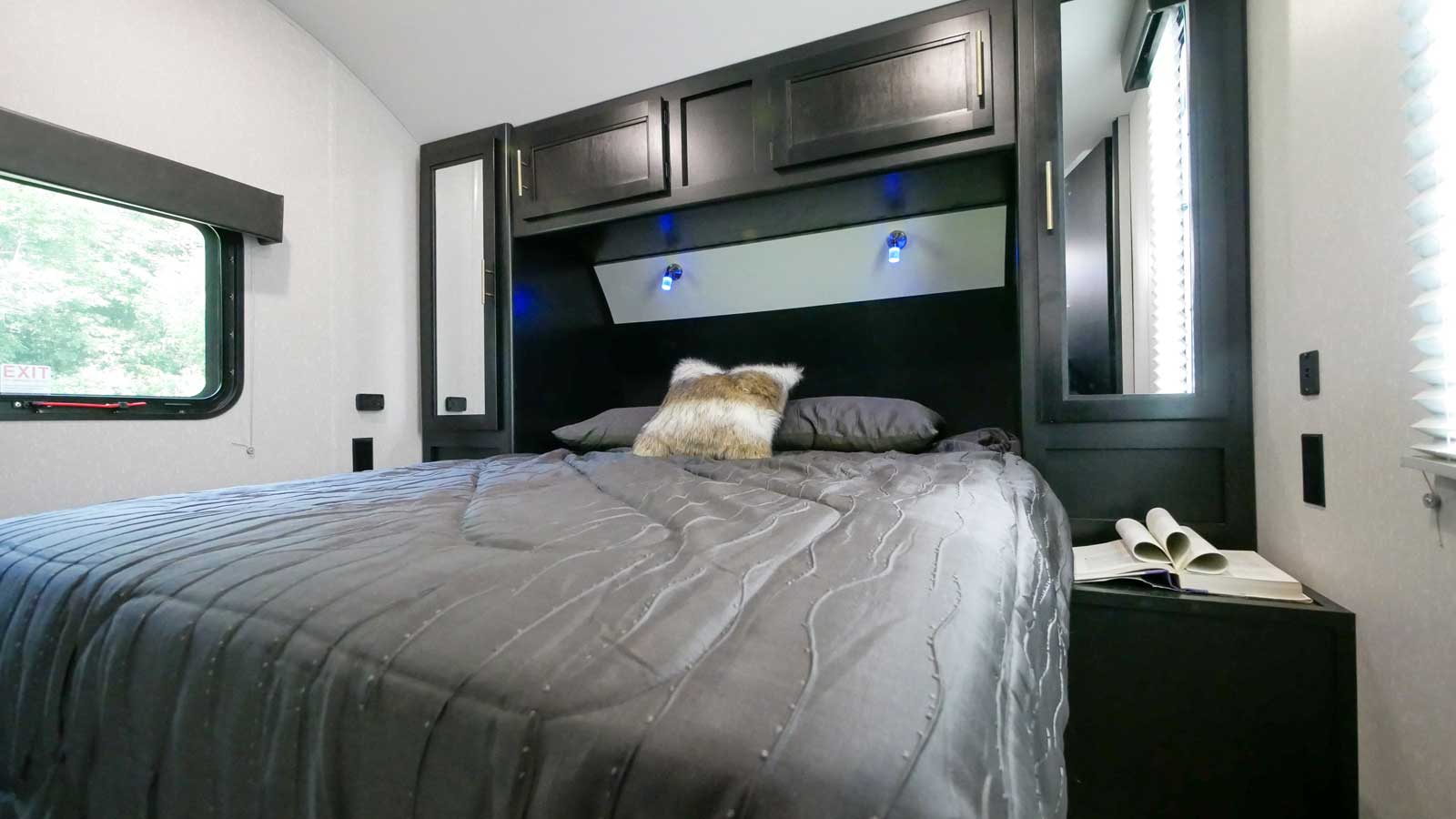 Well-appointed RV rental bedroom: gray bed, built-in storage, blue accent lights, and a window. Ideal for compact living.. Forest River Cherokee Cherokee Black Label 2022