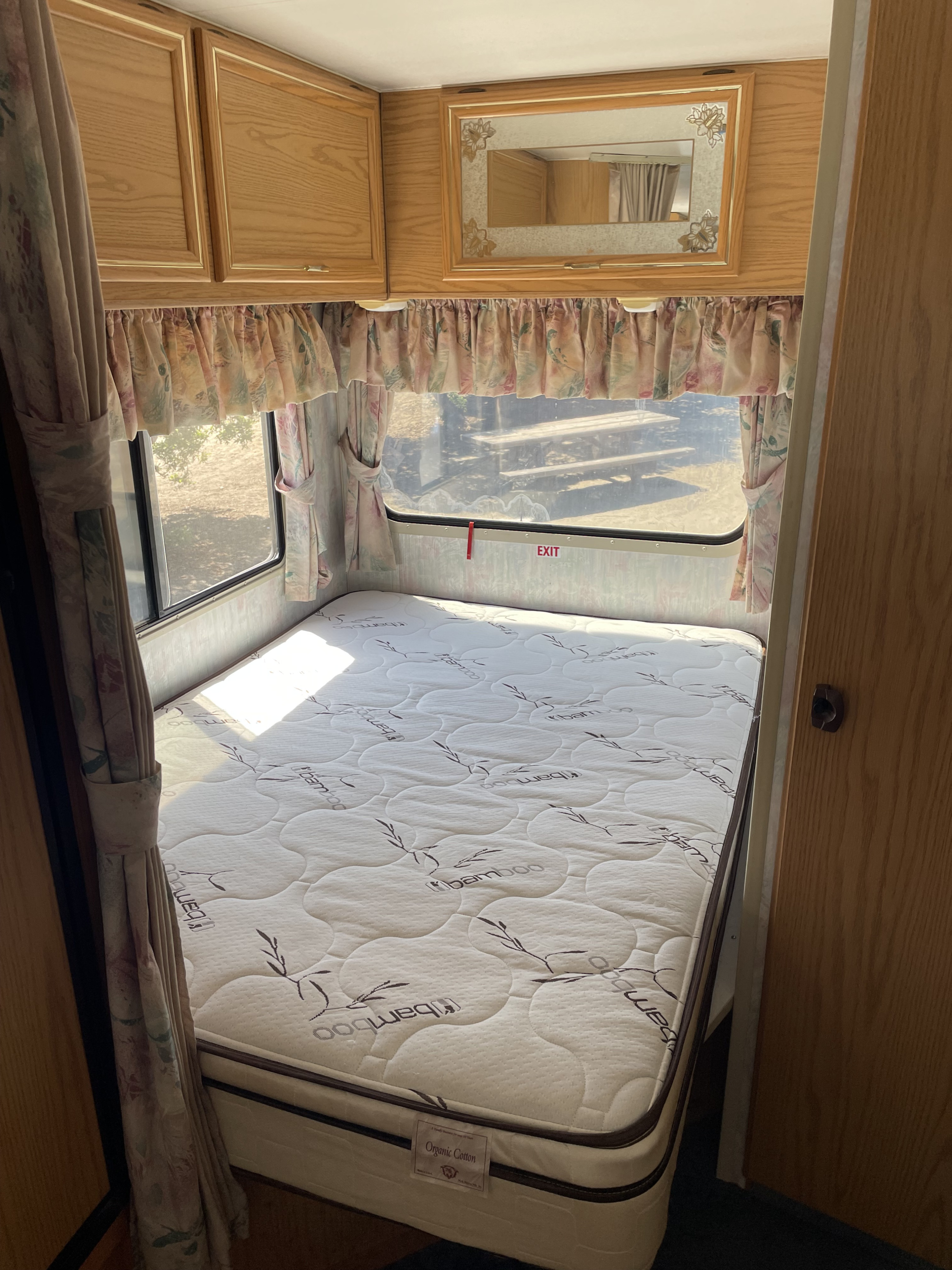Cozy RV rental bedroom featuring a quilted Bamboo mattress, windows with floral curtains, and wooden cabinets.. Itasca Spirit 1995