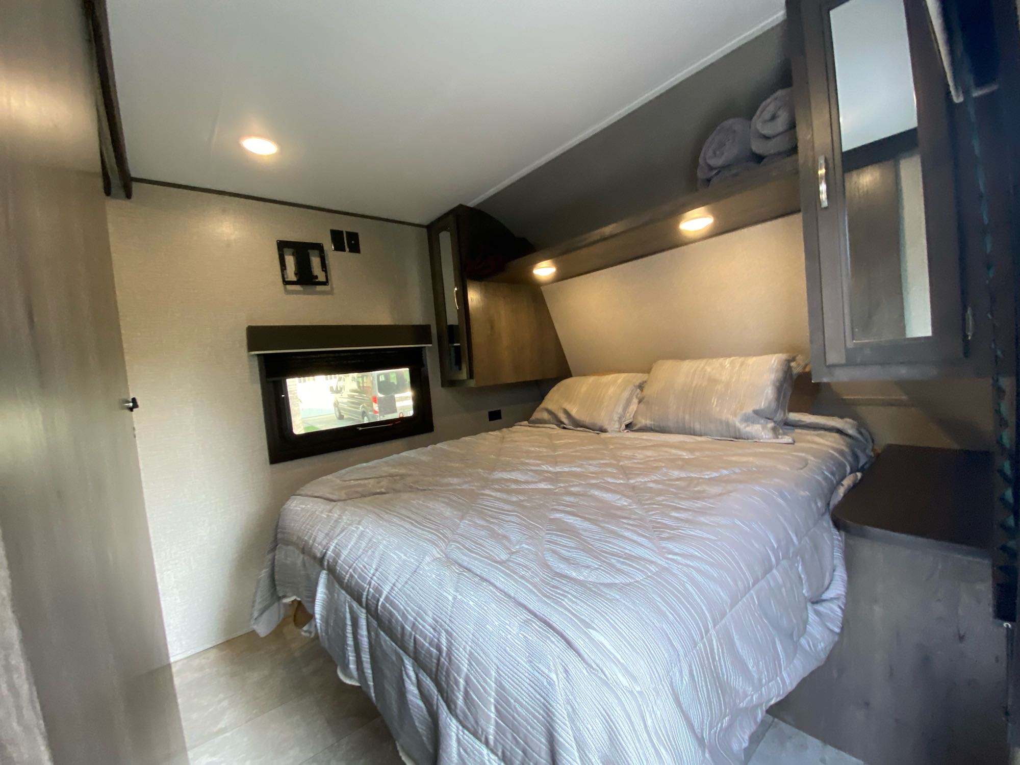 Cozy RV rental bedroom featuring a comfortable bed, window, overhead storage, and a TV mount.. Jayco Jay Flight 2020