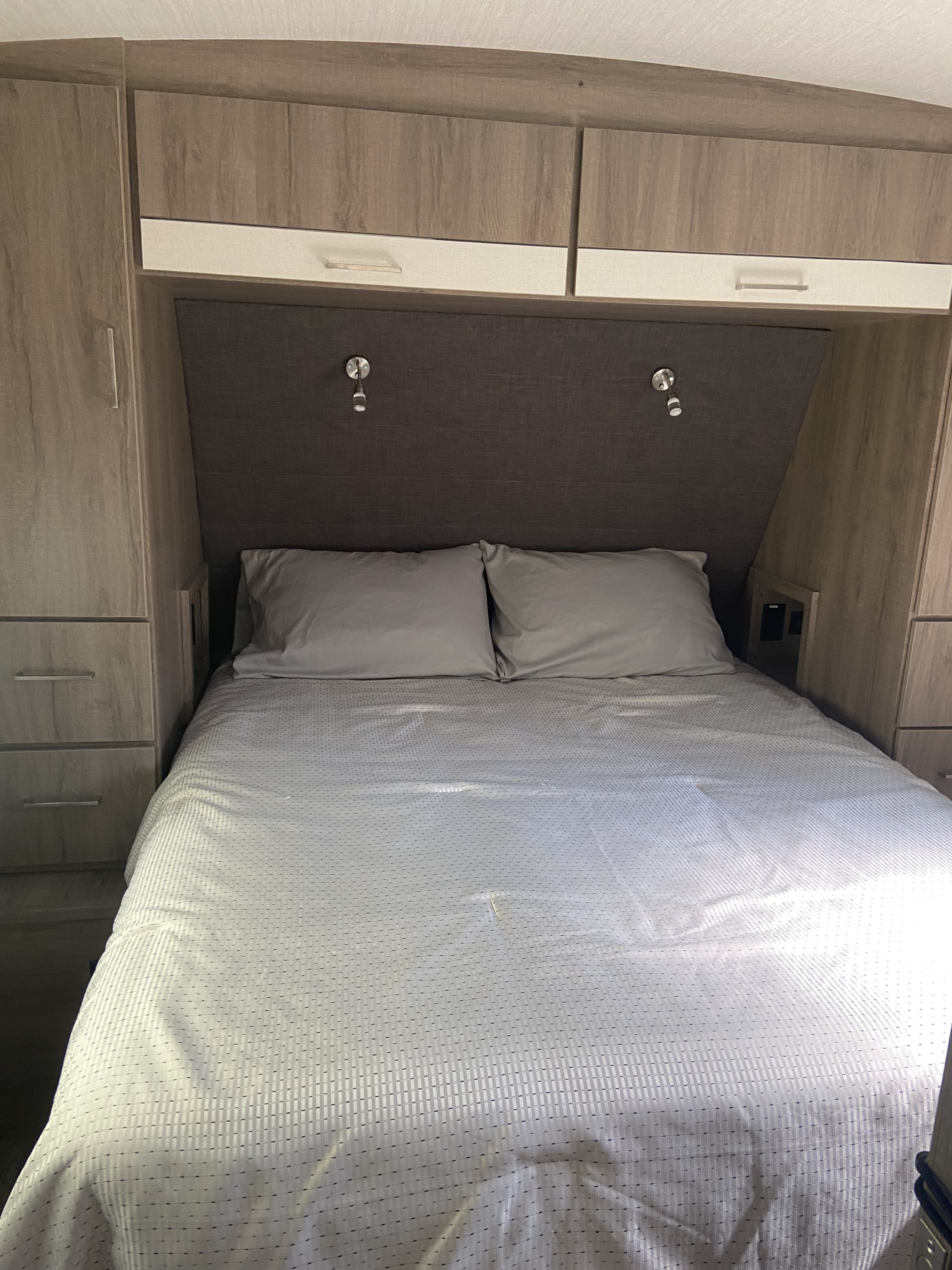 Compact RV rental bedroom showing a comfortable bed, overhead cabinets, and reading lights, ready for your trip.. Grand Design Other 2021