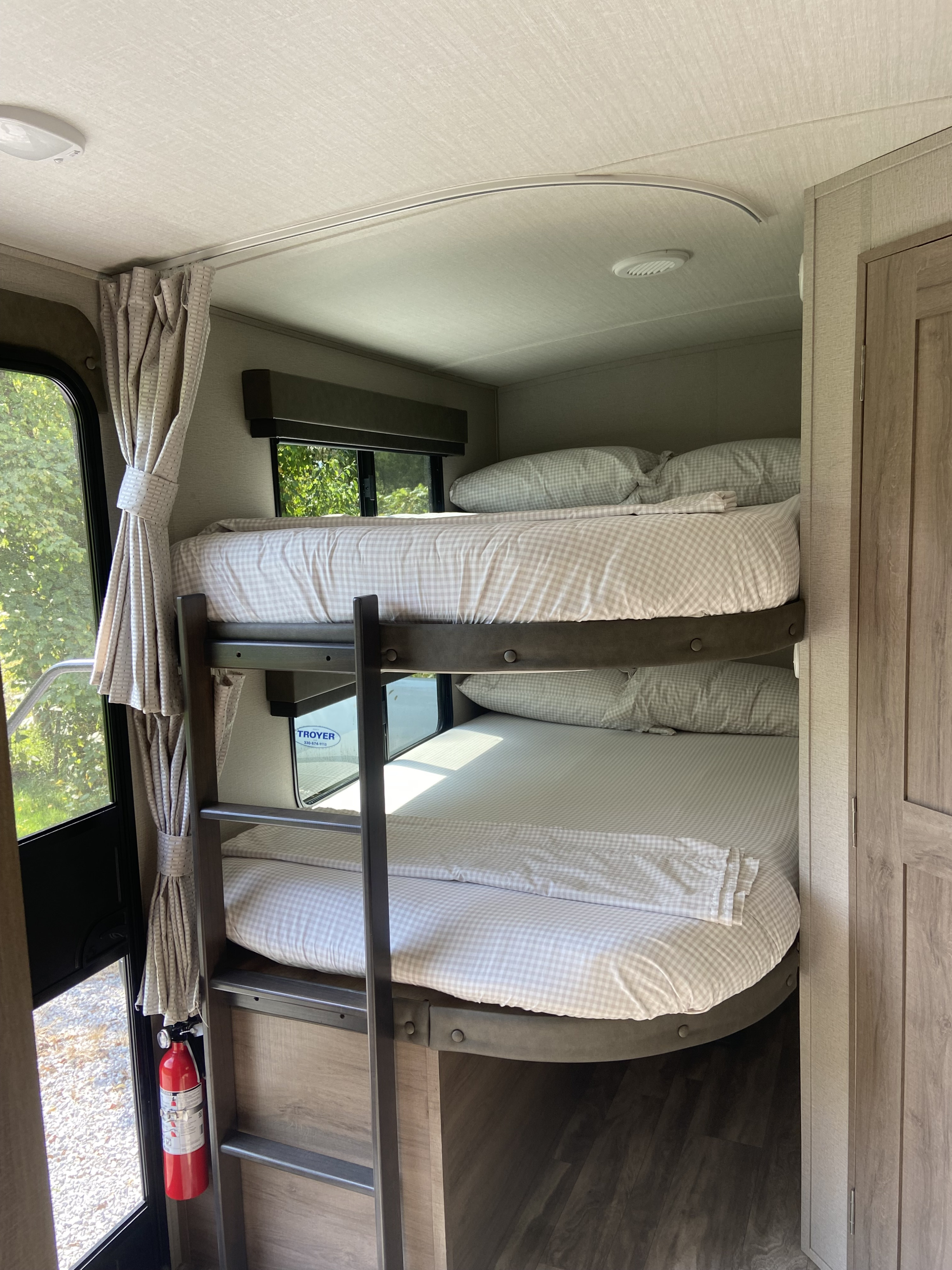 Inside an RV rental: two bunk beds with light checkered bedding, a ladder, and a fire extinguisher.. Grand Design Other 2021