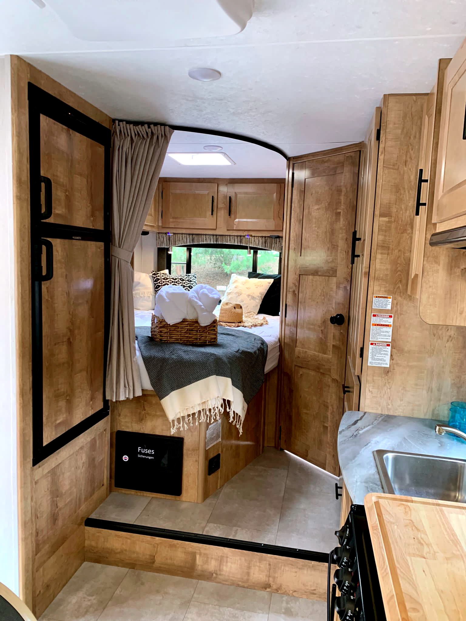 Cozy RV rental interior with bed, kitchen, and warm wood tones, perfect for travel adventures.. Coachmen Leprechaun 2021