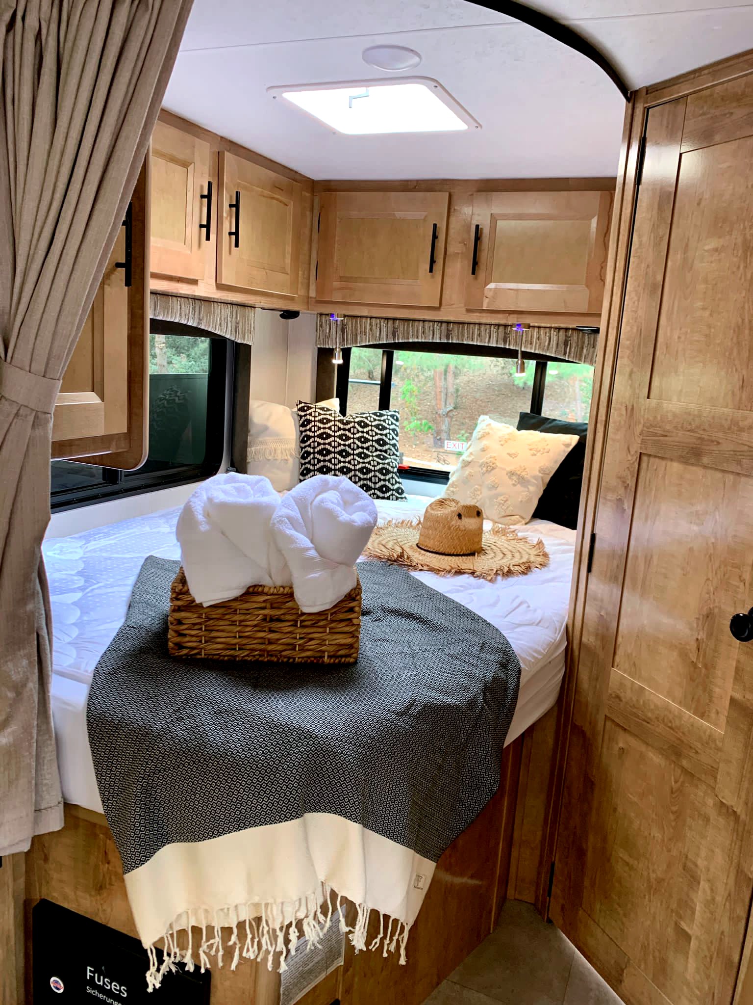 This inviting RV rental bedroom features a comfy bed with towels, wooden cabinets, and large windows.. Coachmen Leprechaun 2021