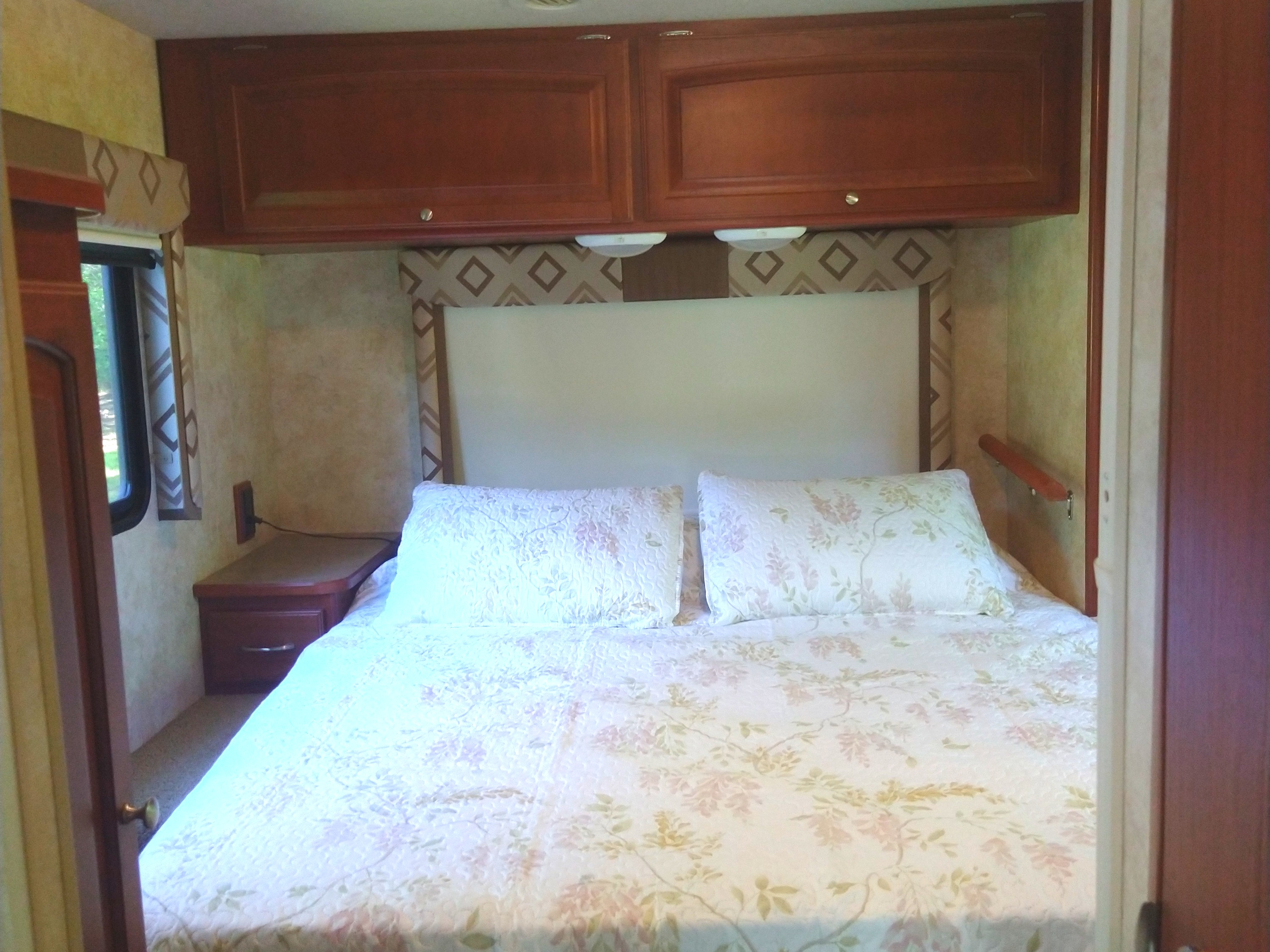 Cozy RV rental bedroom with a comfortable bed, overhead cabinets, and a nightstand, perfect for sleeping on your trip.. Winnebago Access 2011