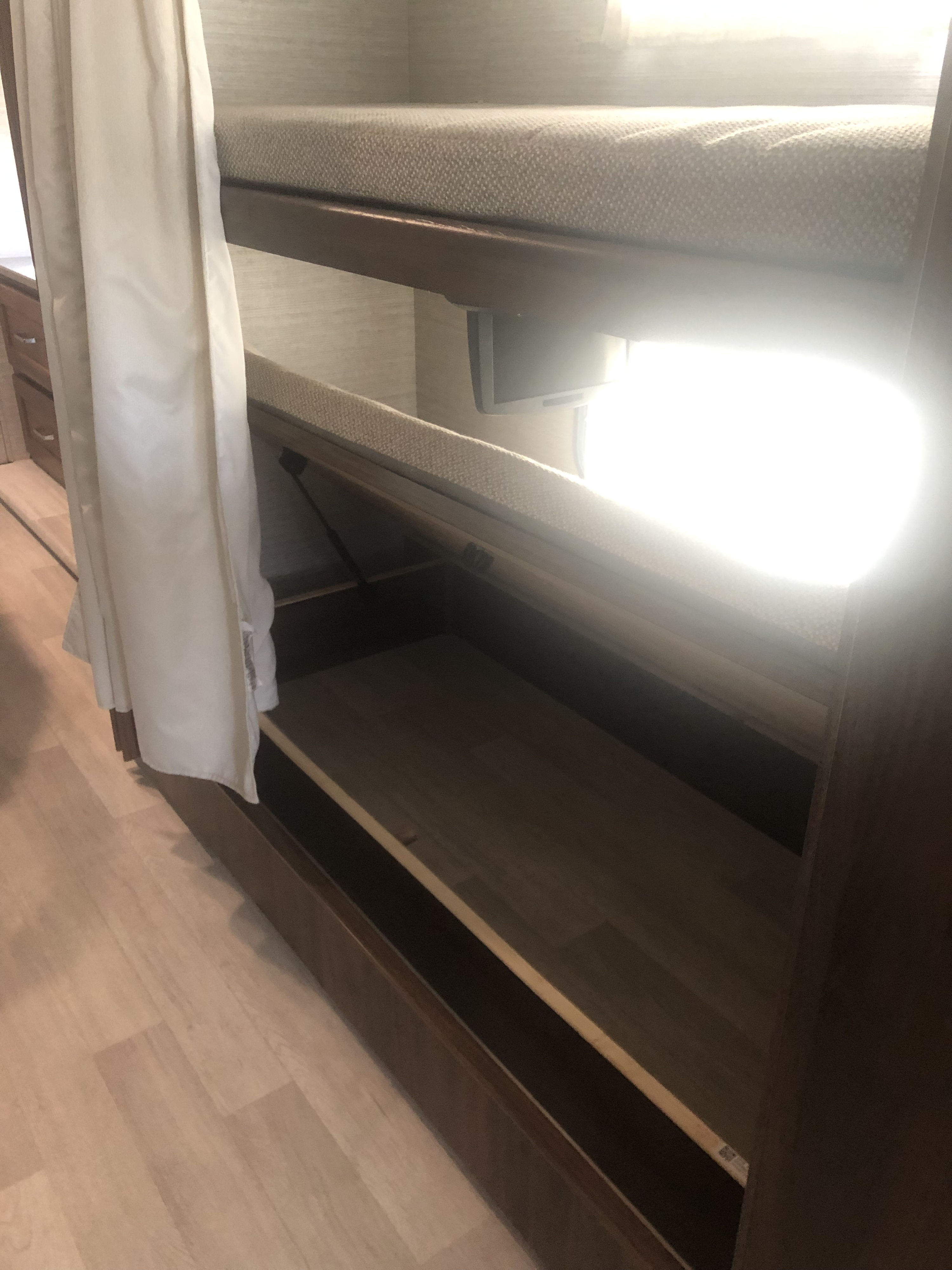 RV rental bunk beds with the lower bed lifted to reveal storage underneath, featuring a privacy curtain in a bright interior.. Winnebago Vista 2022