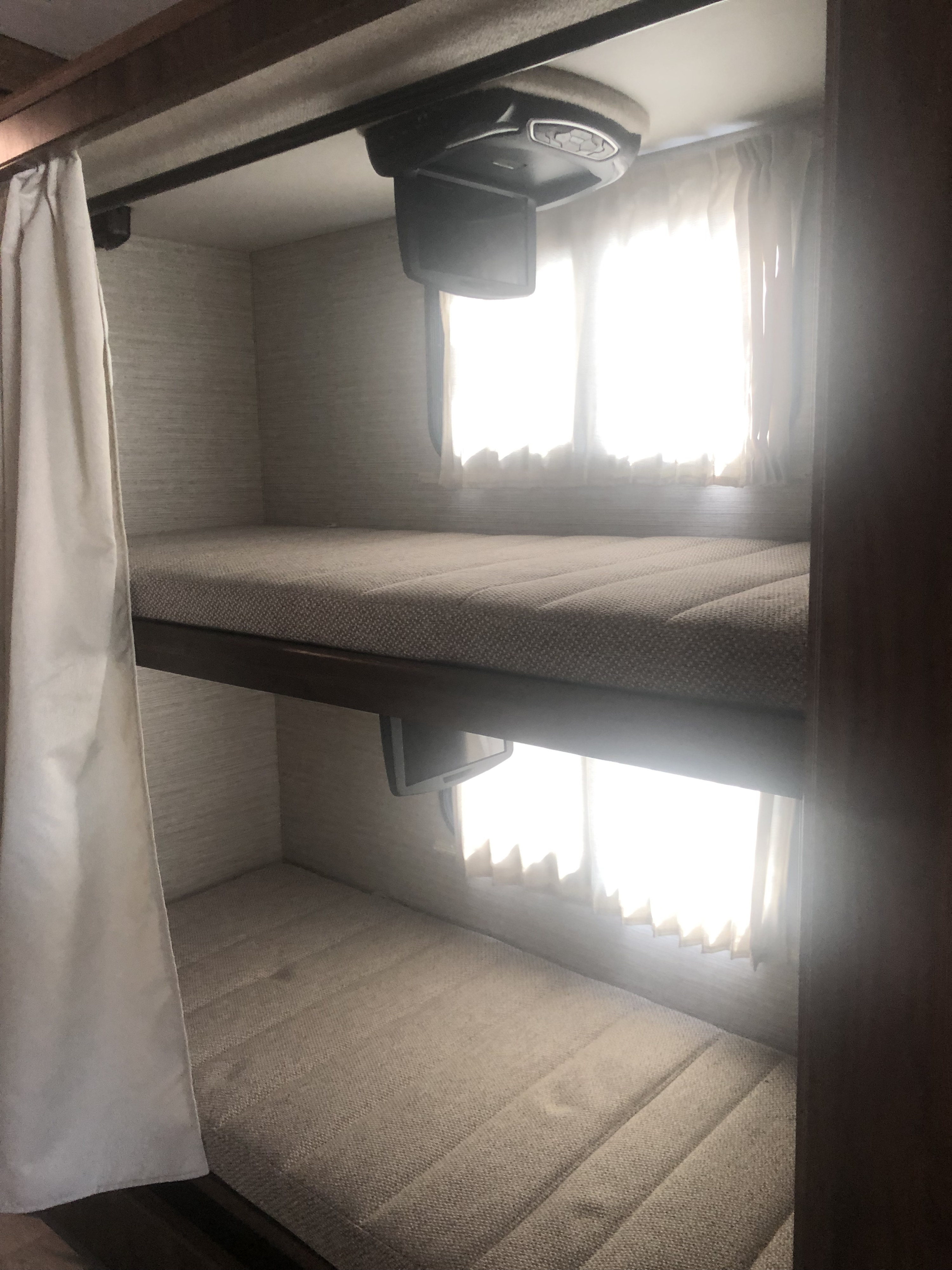Comfortable bunk beds in an RV rental, featuring a flip-down TV and bright windows. Ideal for mobile living.. Winnebago Vista 2022