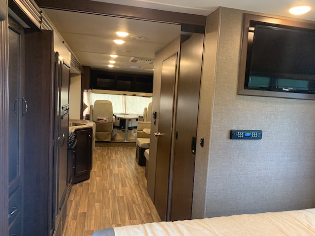 Explore this RV rental interior: bedroom with TV, adjacent kitchen, and a dining area with wood-look flooring.. Thor Motor Coach A.C.E 2017