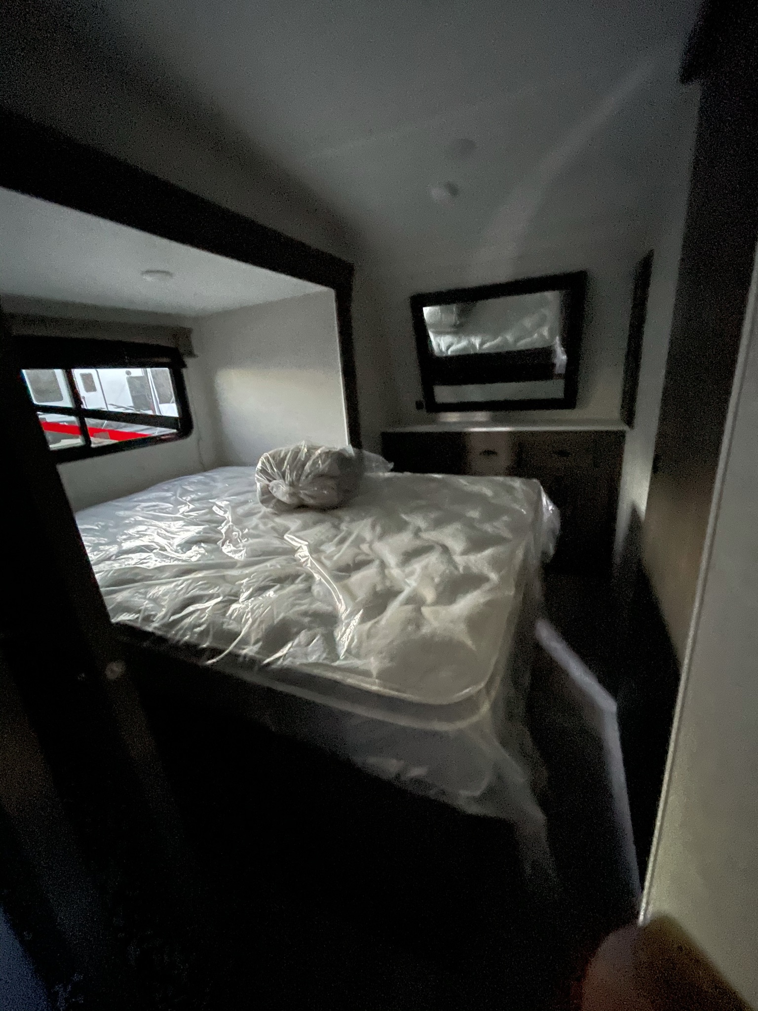 Clean RV rental bedroom featuring a plastic-wrapped mattress, dresser with mirror, and window view.. Forest River Shockwave 2021