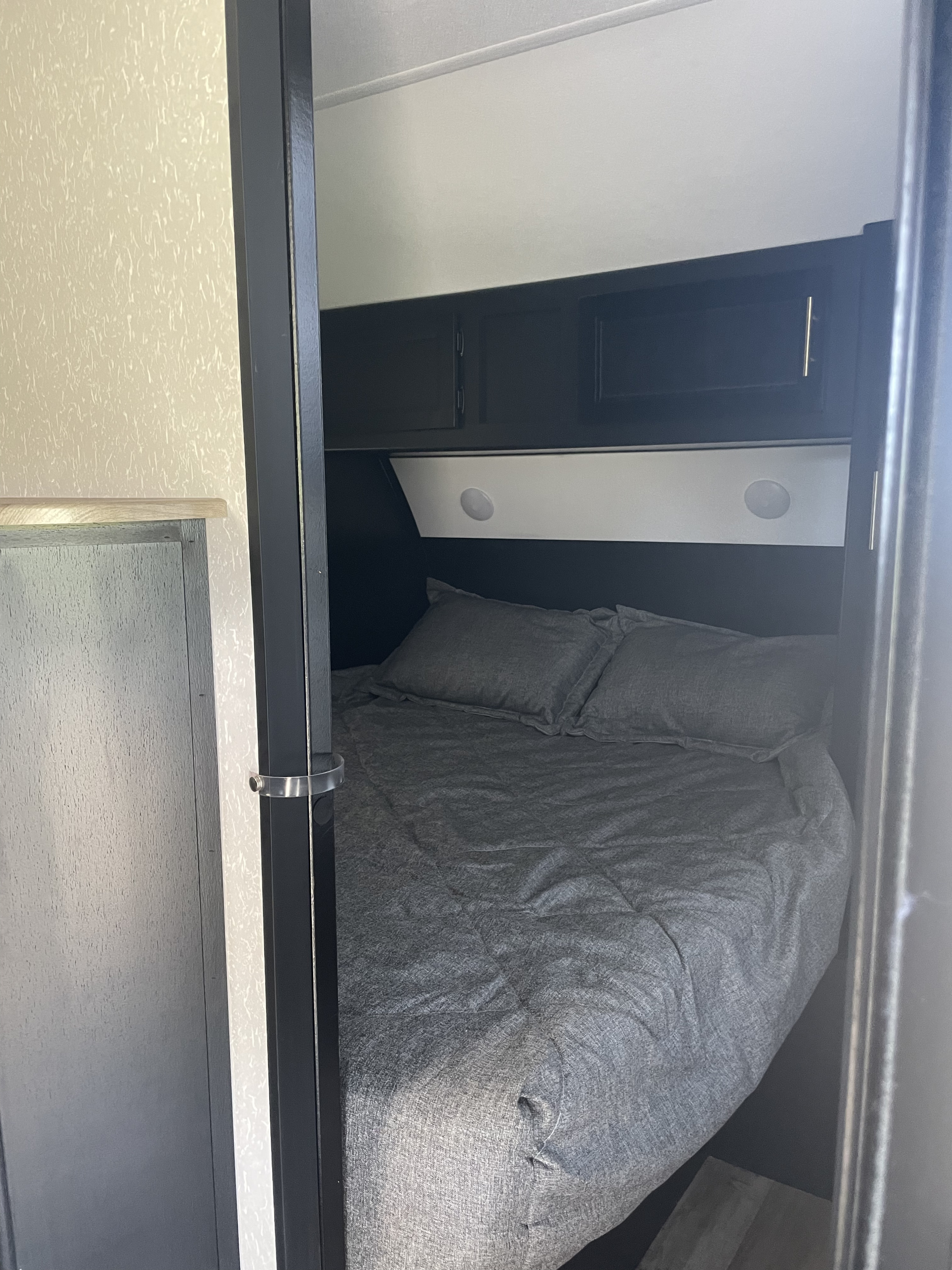Cozy RV rental bedroom with gray bedding, overhead cabinets, and built-in lighting, perfect for your next adventure.. Forest River Cherokee Grey Wolf 2022