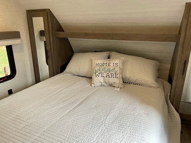 Cozy RV rental bedroom with a bed, light bedding, and a "Home is wherever we are" pillow. Ideal for travel trailer stays.. Forest River Wildwood X-Lite 2022