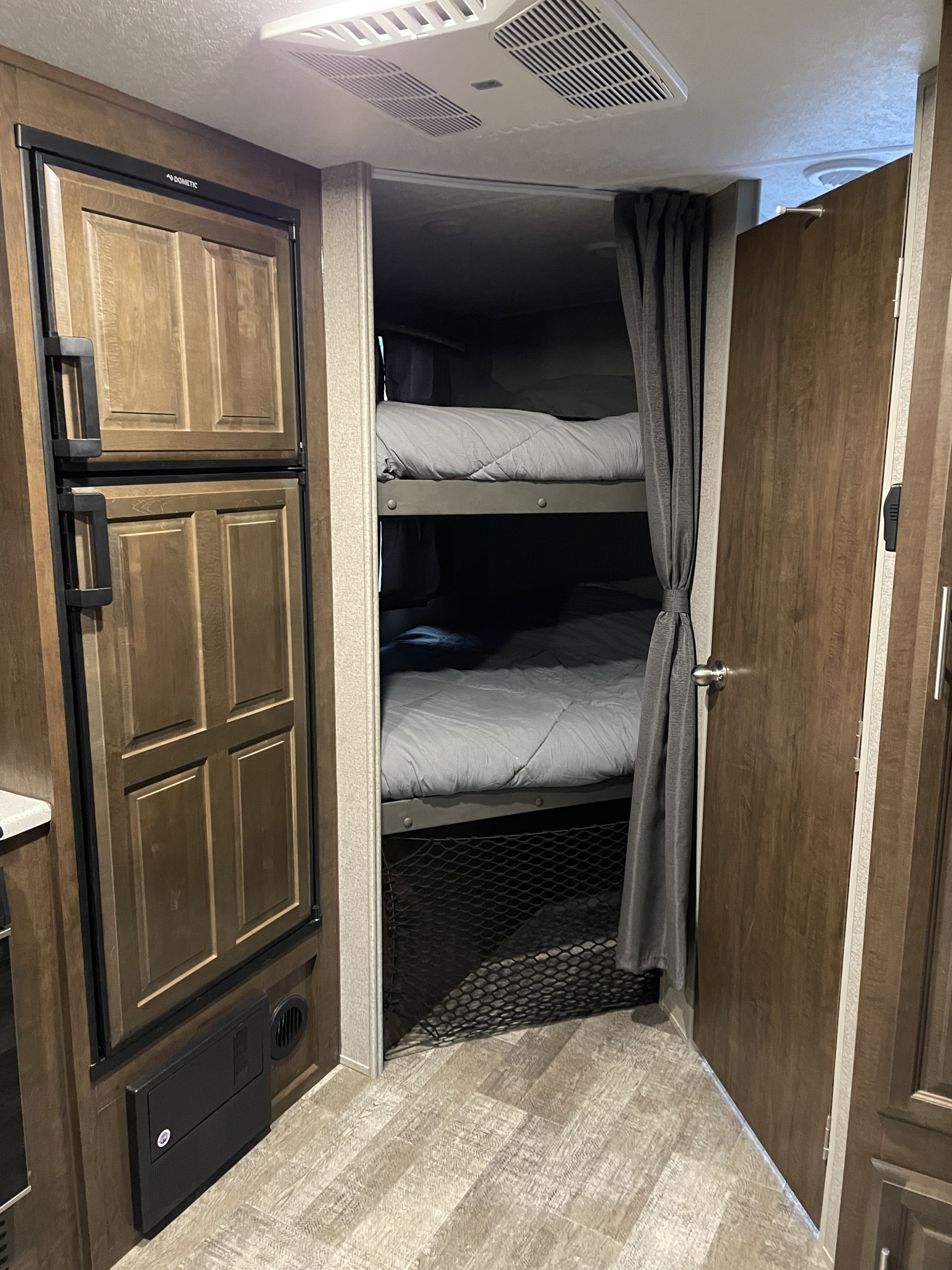 RV rental interior features bunk beds with gray bedding, a wood-paneled Dometic fridge, and a compact layout.. Forest River Rockwood Mini Lite 2020
