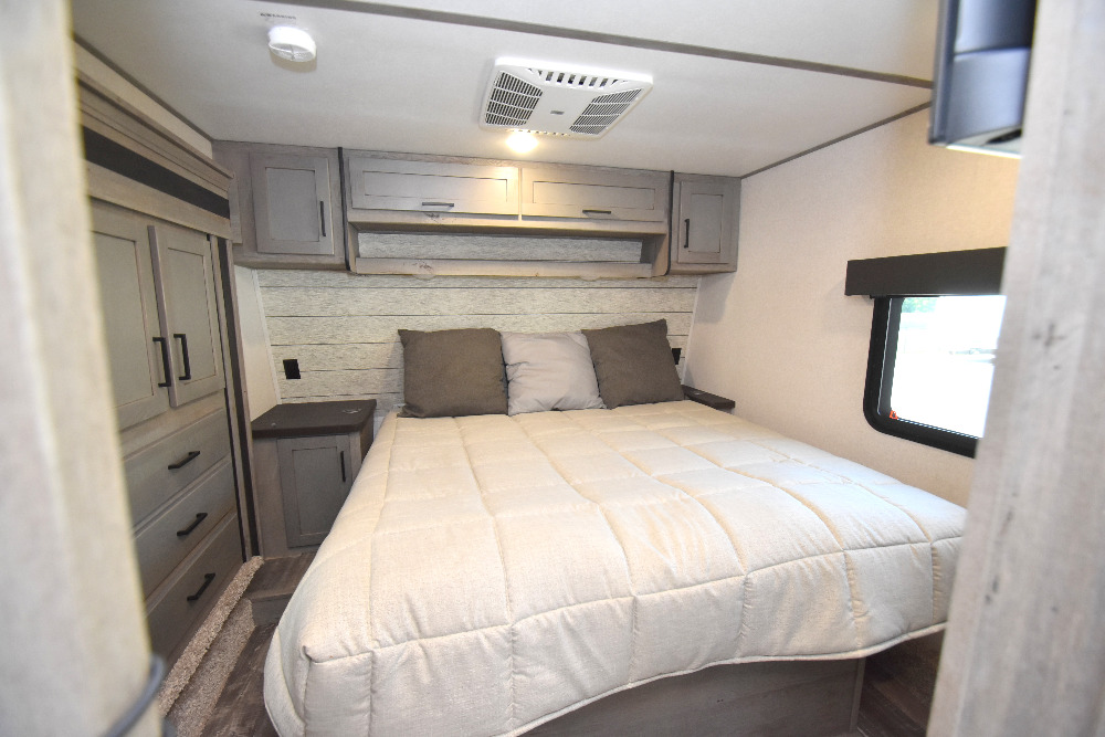 Comfortable RV rental bedroom with a queen bed, overhead cabinets, wardrobe, AC unit, and window.. Keystone Raptor 2023