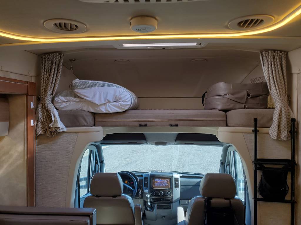 RV rental: Interior shows a comfortable cab-over bunk with bedding, tied-back curtains, and the front cockpit area.. Winnebago View 2018