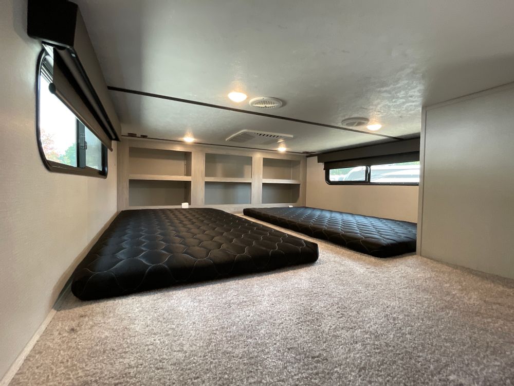 Explore this RV rental's spacious bunk room. Two mattresses, shelving, and windows offer comfy travel accommodation.. Keystone Montana High Country 2022