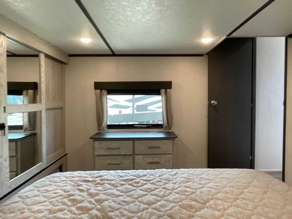 Experience comfort in this RV rental bedroom, featuring a quilted bed, dresser, window, and mirrored wardrobe.. Keystone Montana High Country 2022