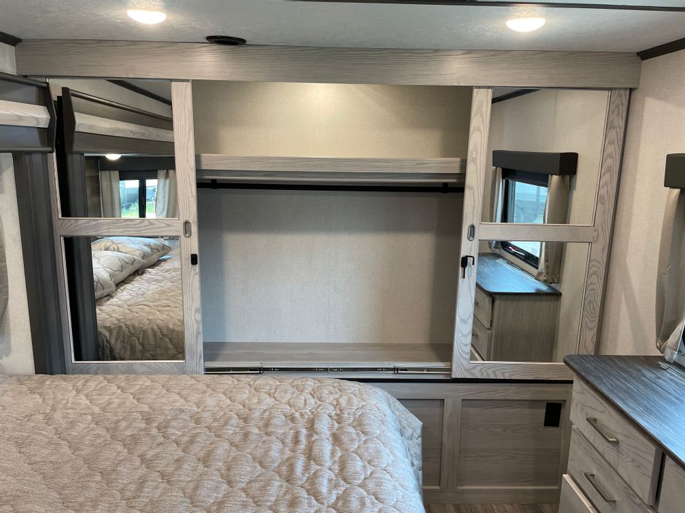 This RV rental bedroom offers a comfortable bed and a mirrored wardrobe, maximizing storage and space in compact RV living.. Keystone Montana High Country 2022