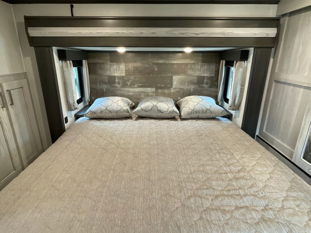 Comfortable RV rental bedroom featuring a large bed, stylish wood-paneled headboard, and convenient built-in storage.. Keystone Montana High Country 2022