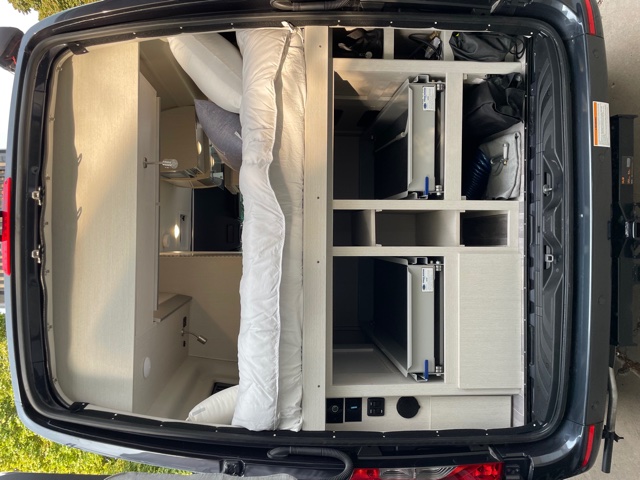 Inside an **RV rental** conversion van: a cozy bed and efficient storage system viewed from the rear, perfect for road trips.. Mercedes-Benz 4x4 Sprinter mwb 2021