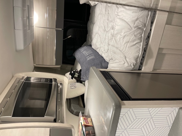 Cozy rv rental interior featuring a compact kitchen with a microwave and cooktop, plus a comfortable bed with white bedding.. Mercedes-Benz 4x4 Sprinter mwb 2021