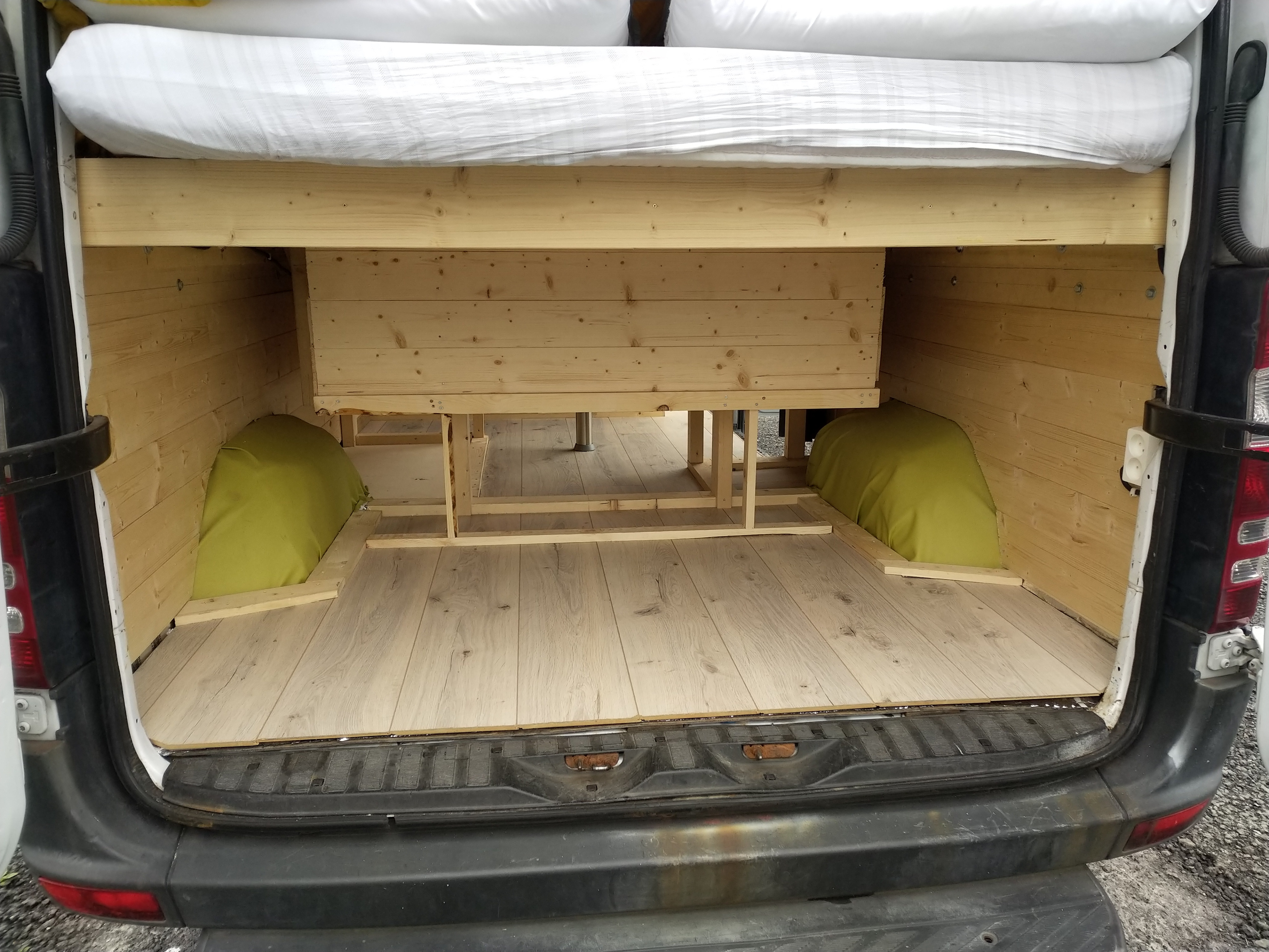 Looking into the rear of an RV rental van, showcasing a wooden bed frame, under-bed storage, and wood-paneled interior.. Mercedes-Benz Sprinter 2008