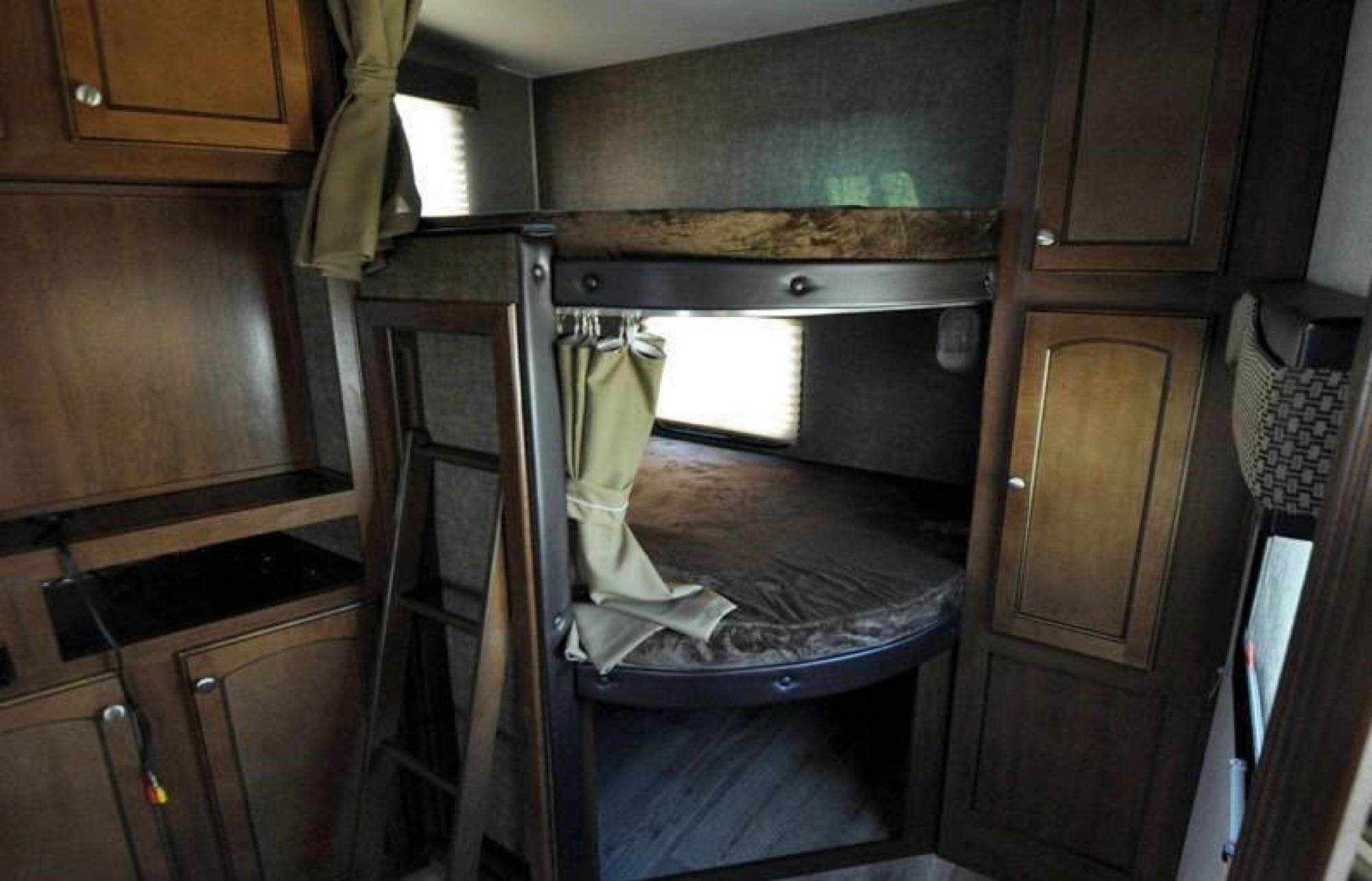 RV rental bedroom featuring sturdy bunk beds, a ladder, privacy curtain, and dark wood cabinetry with storage.. Heartland Elkridge 2016