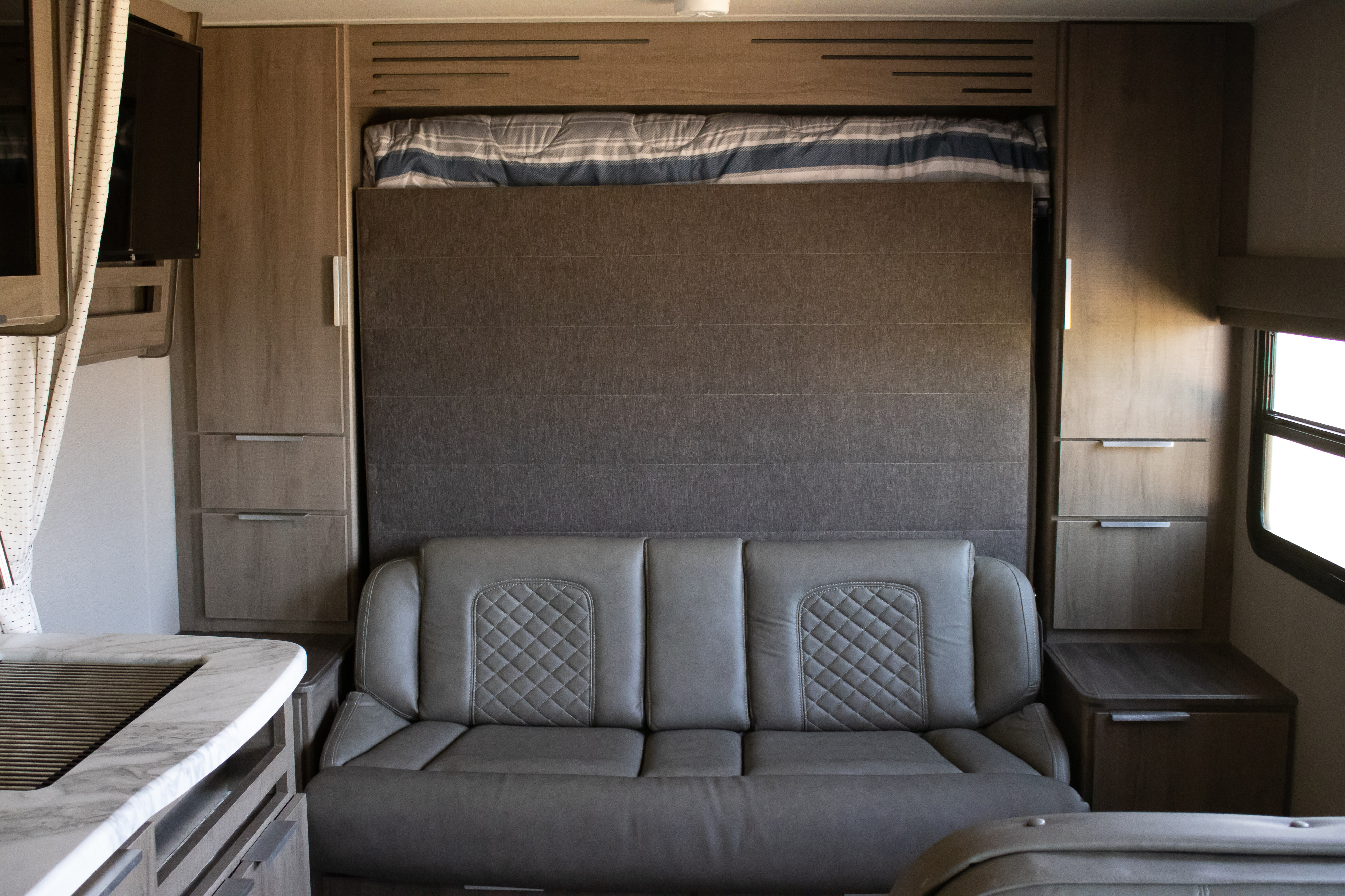 RV rental interior: A stylish grey sofa and a space-saving Murphy bed are ready for use in this compact living area.. Grand Design Imagine XLS 2021