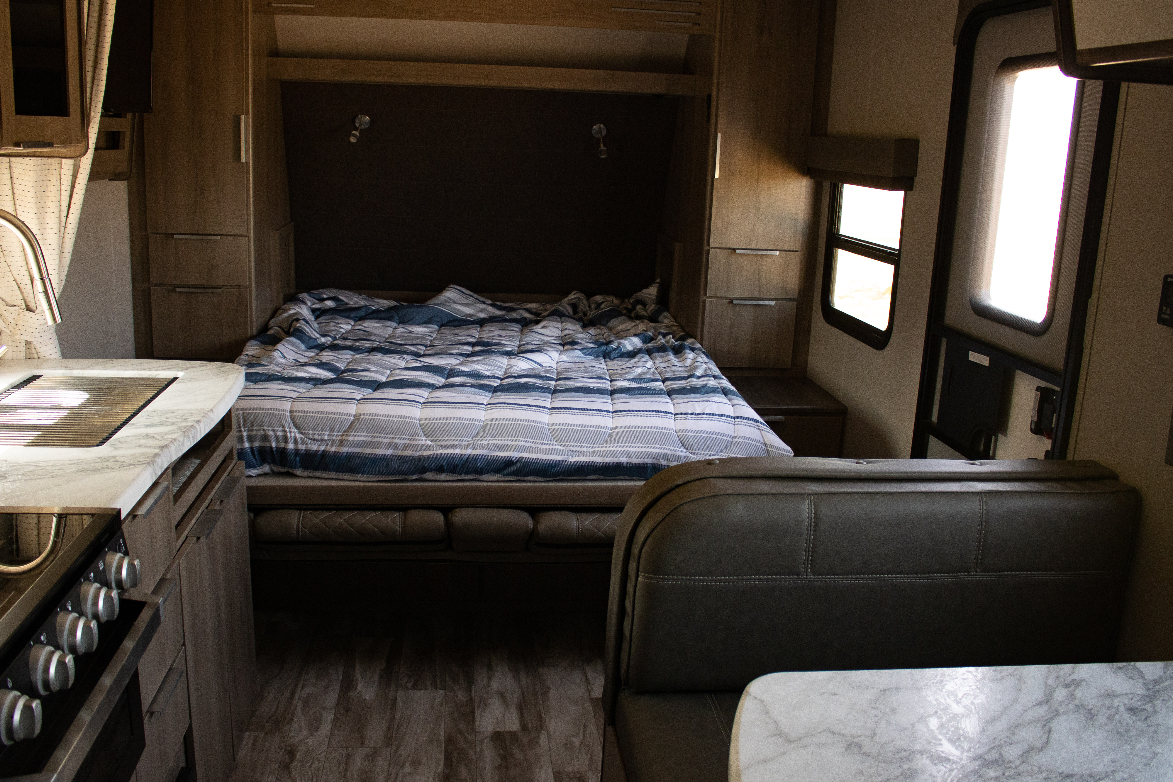 Cozy rv rental interior featuring a compact kitchen, bed with striped comforter, and dinette seating.. Grand Design Imagine XLS 2021