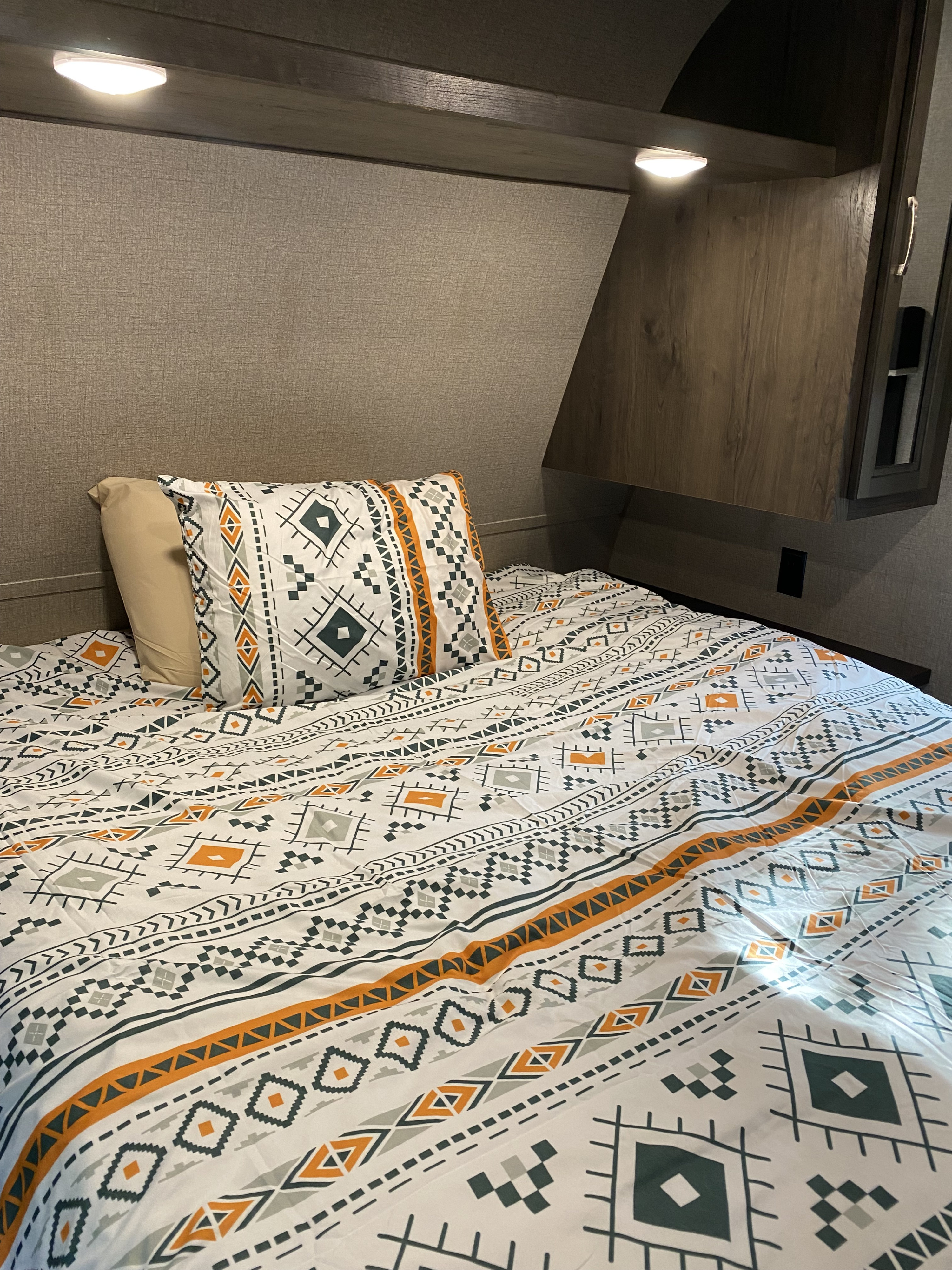 An inviting RV rental bedroom. The bed has white, orange & grey geometric bedding. Features overhead lighting & dark wood built-ins.. Jayco Jay Flight 2020