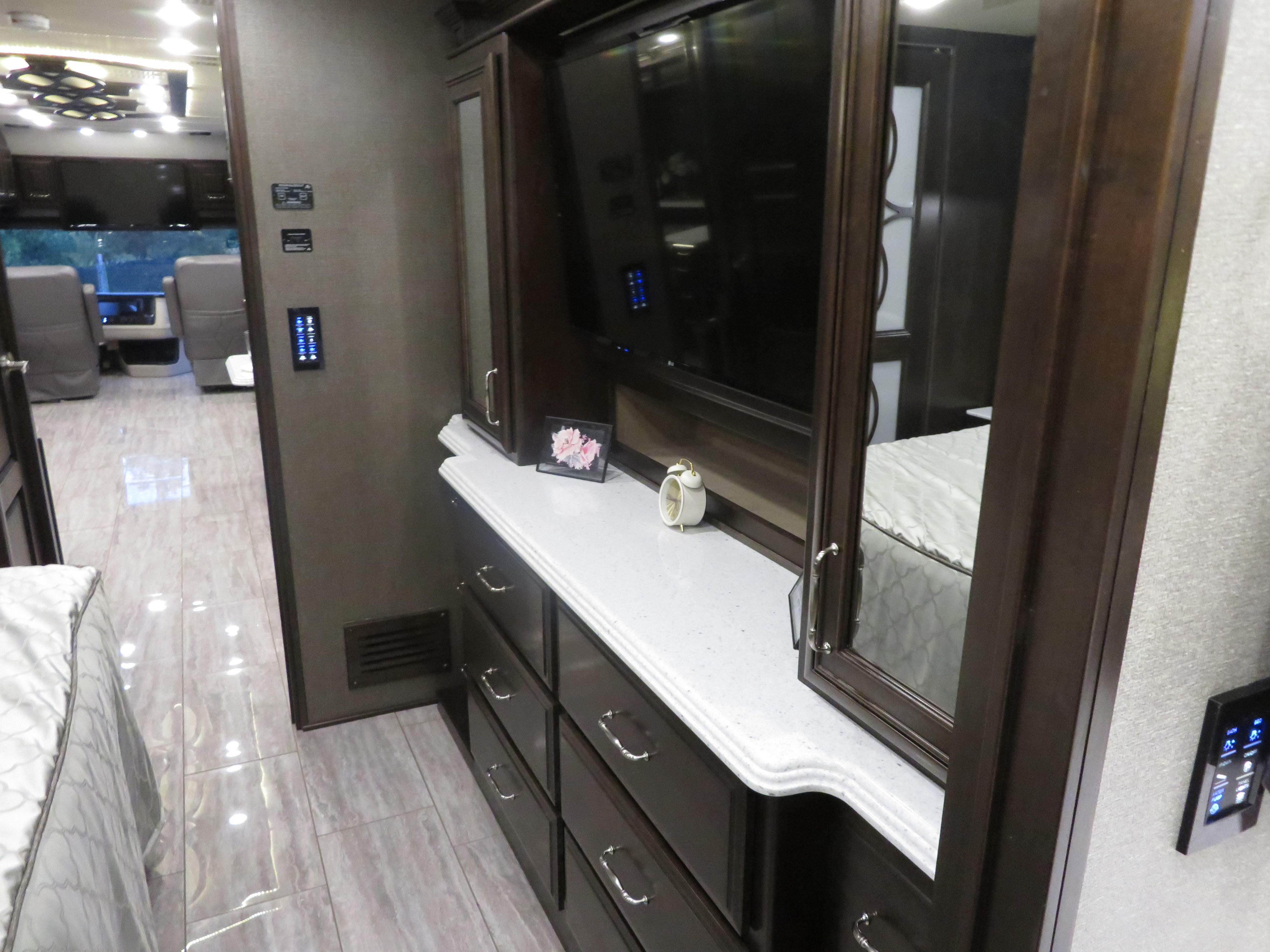 Modern RV rental interior, showcasing a bedroom with TV, sleek dresser, tiled floor, and digital control panels.. Monaco Signature 2019