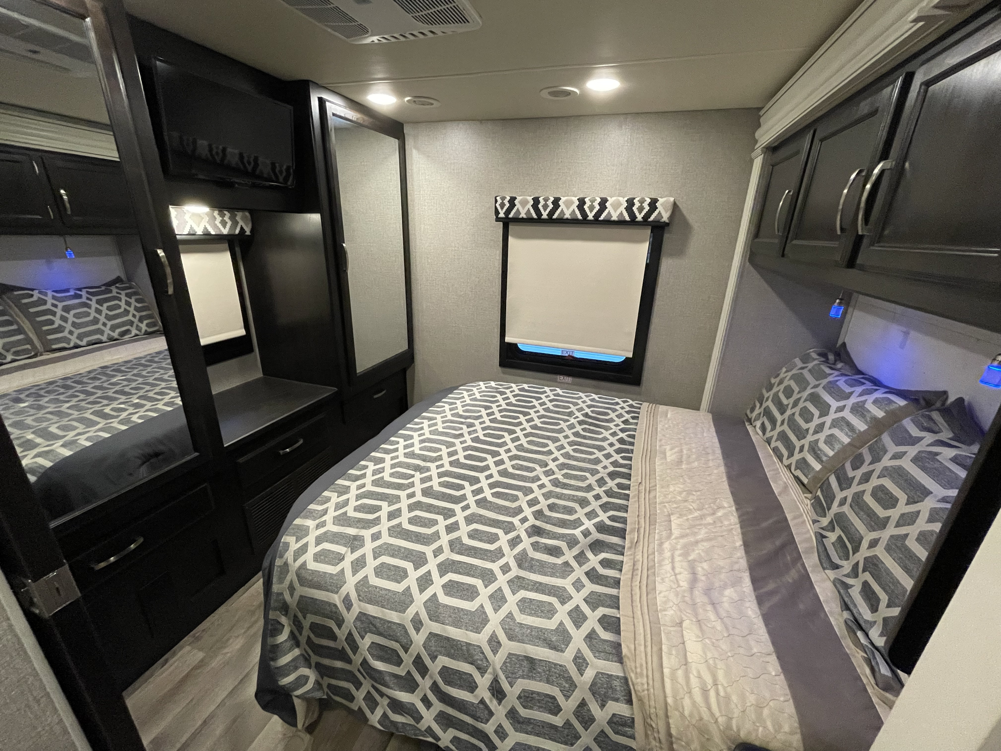 Cozy RV rental bedroom with modern gray patterned bedding, TV, mirror, and storage cabinets for travel comfort.. Jayco Greyhawk 2020