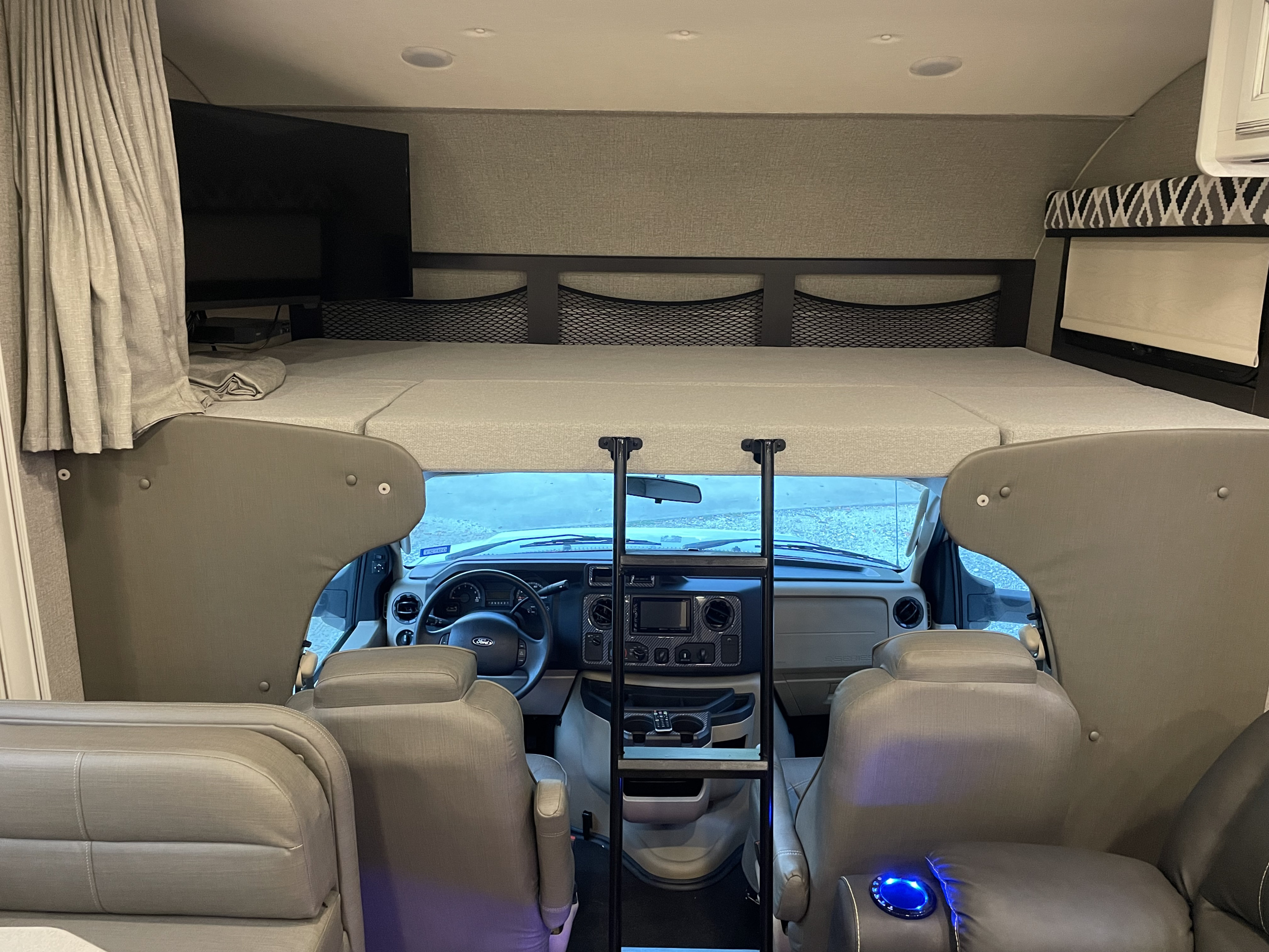 View from an RV rental's living area into the front cab, featuring an overhead bunk bed & driver cockpit.. Jayco Greyhawk 2020