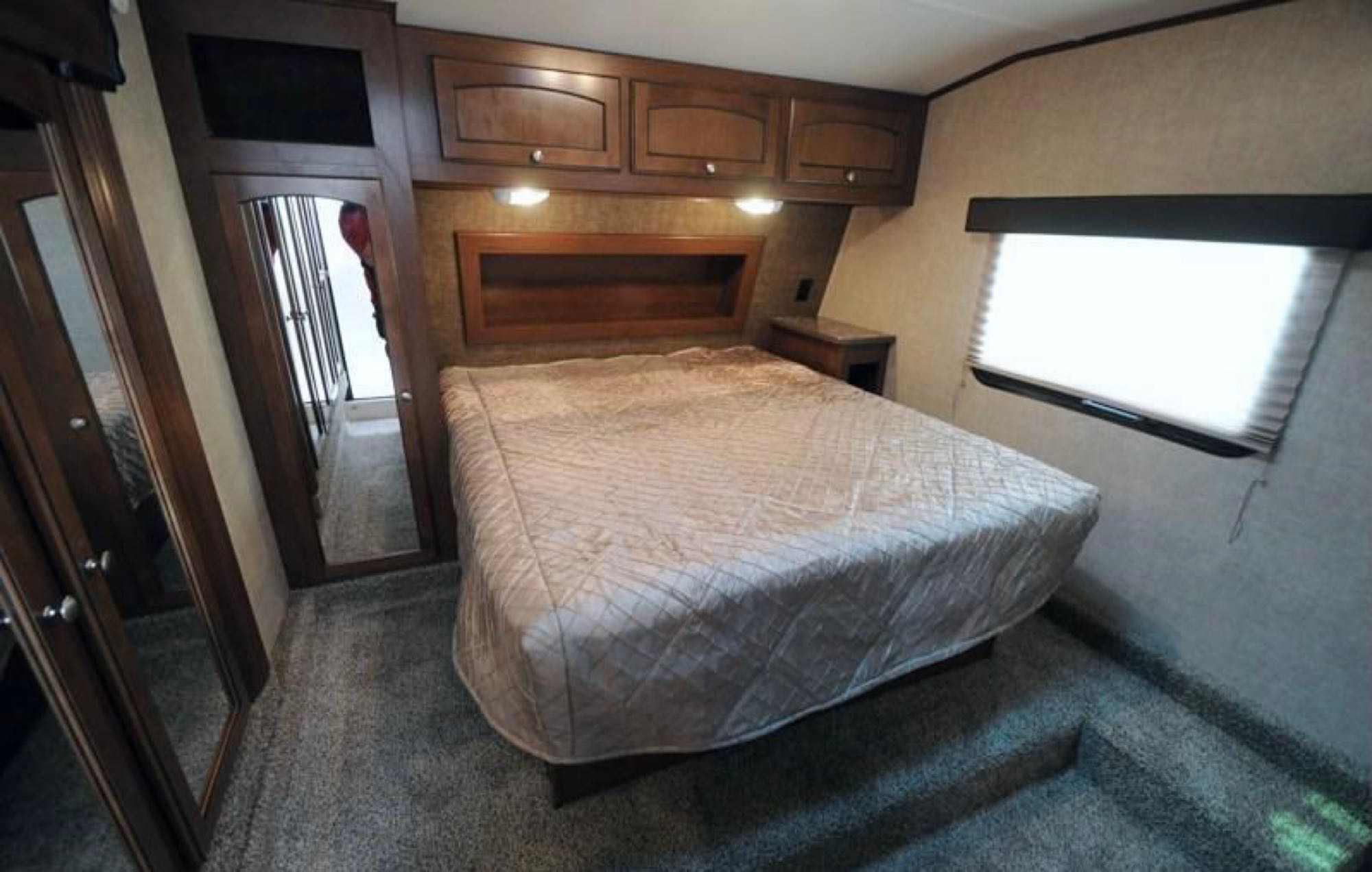 Cozy RV rental bedroom featuring a comfortable bed, mirrored closets, overhead cabinets, and a bright window.. Heartland Elkridge 2016