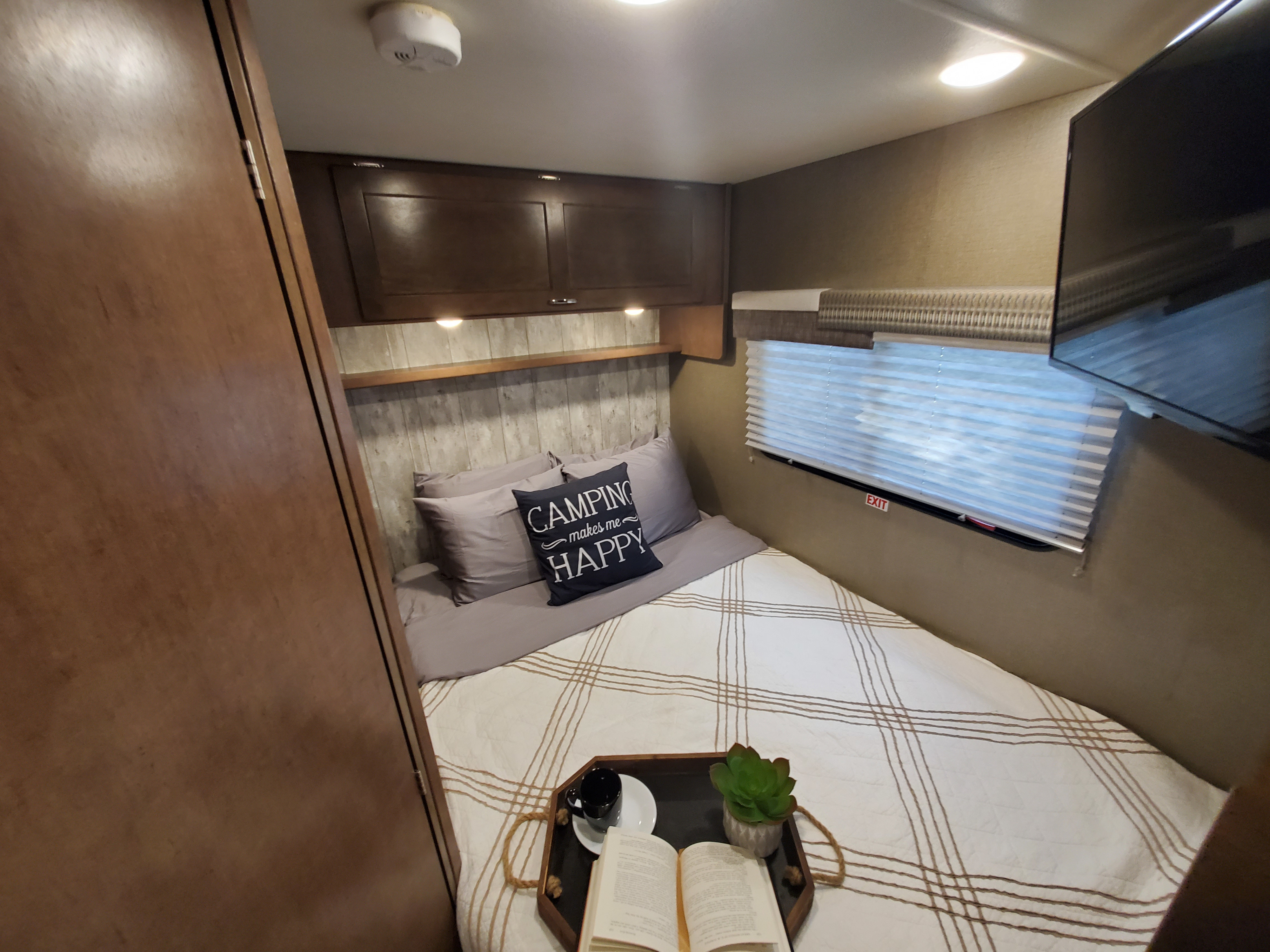 RV rental bedroom with a cozy bed, "CAMPING makes me HAPPY" pillow, and a tray with a book & coffee for your retreat.. Winnebago Outlook 2019