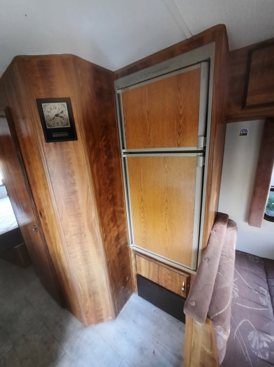 Cozy RV rental interior, featuring wood paneling, a classic refrigerator, and a bed. Ideal for your next adventure.. Ford Econoline 1986