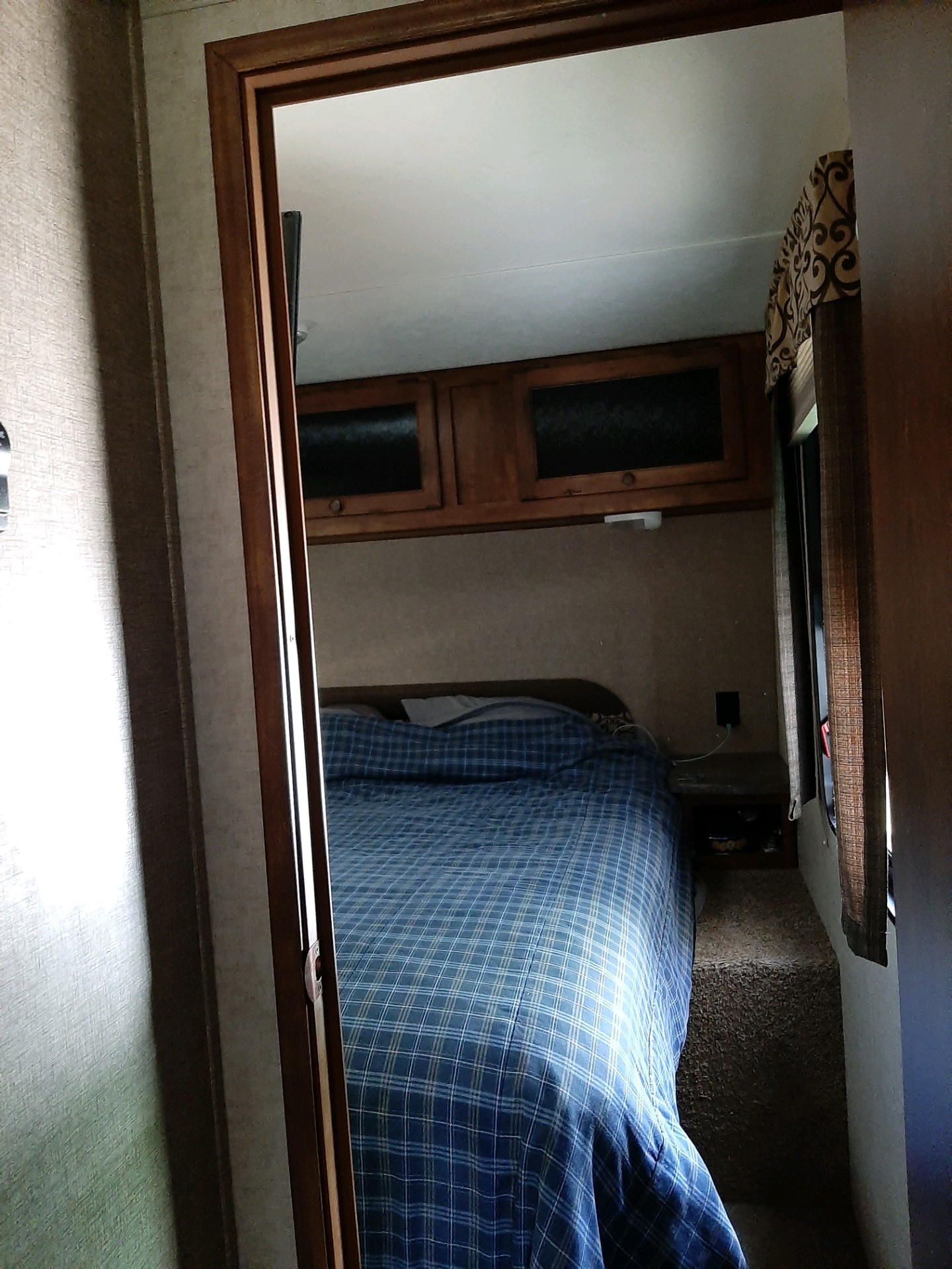 Cozy RV rental bedroom with blue plaid bedding, overhead storage, and a nightstand, offering a compact interior.. Keystone Sprinter 2014