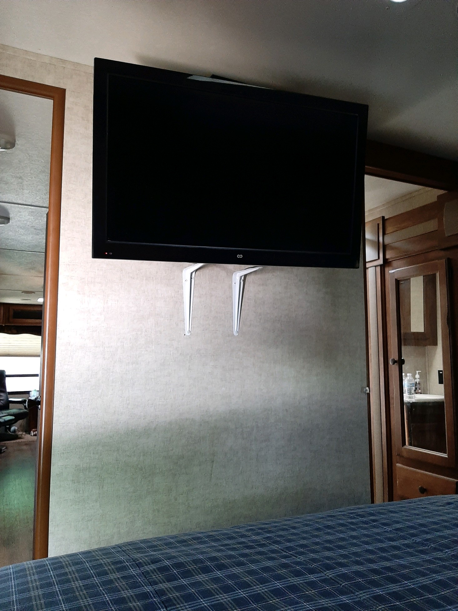 Inside an RV rental: a modern TV is wall-mounted in the bedroom, above a blue checkered bed, next to wooden cabinets.. Keystone Sprinter 2014