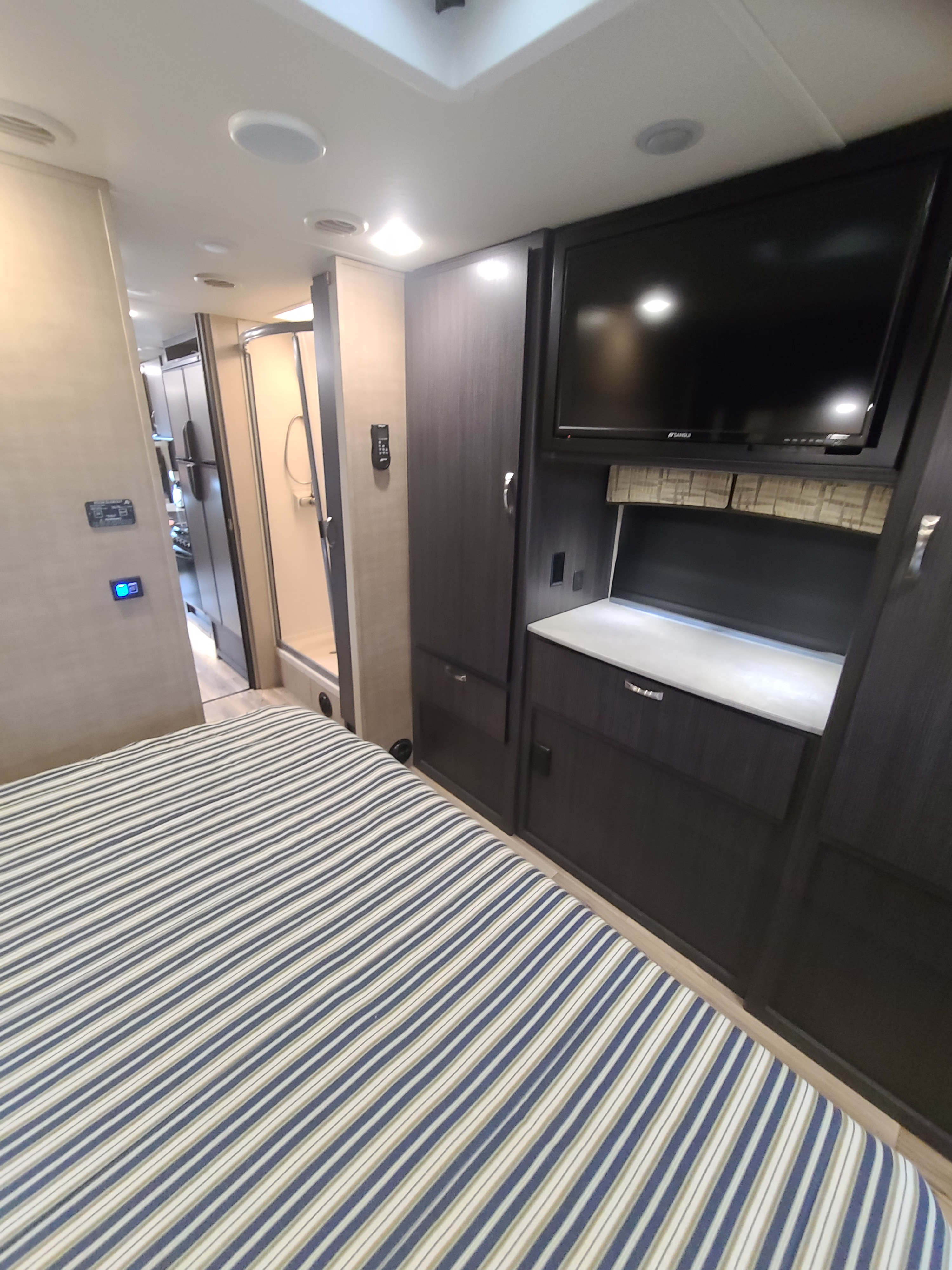 RV rental bedroom: Striped bedding, TV, sleek cabinets, and hallway to shower.. Dynamax Isata 2018