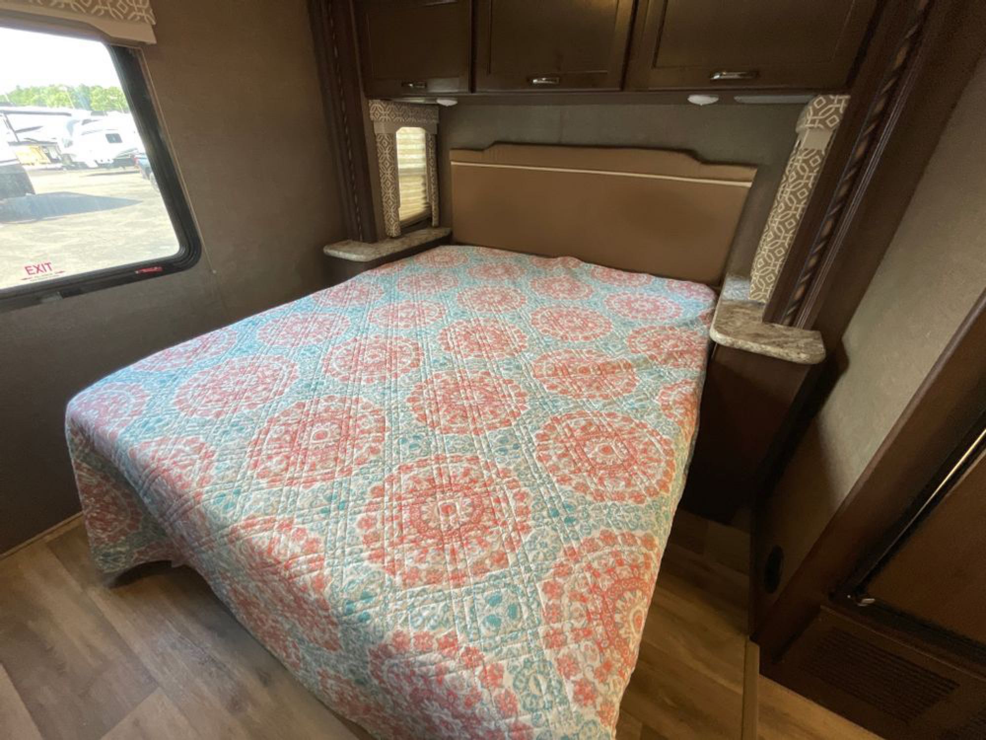 Explore this spacious RV rental bedroom featuring a vibrant quilt, ample storage cabinets, and a window for natural light.. Thor Motor Coach Freedom Elite 2017