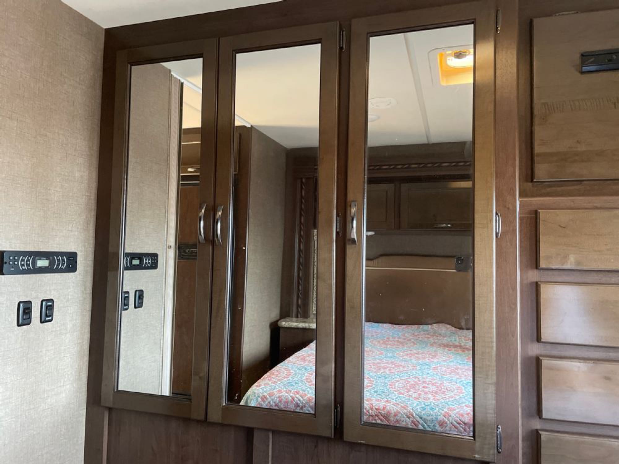 RV rental interior featuring mirrored cabinets reflecting a cozy bedroom, alongside wall controls & wooden drawers.. Thor Motor Coach Freedom Elite 2017