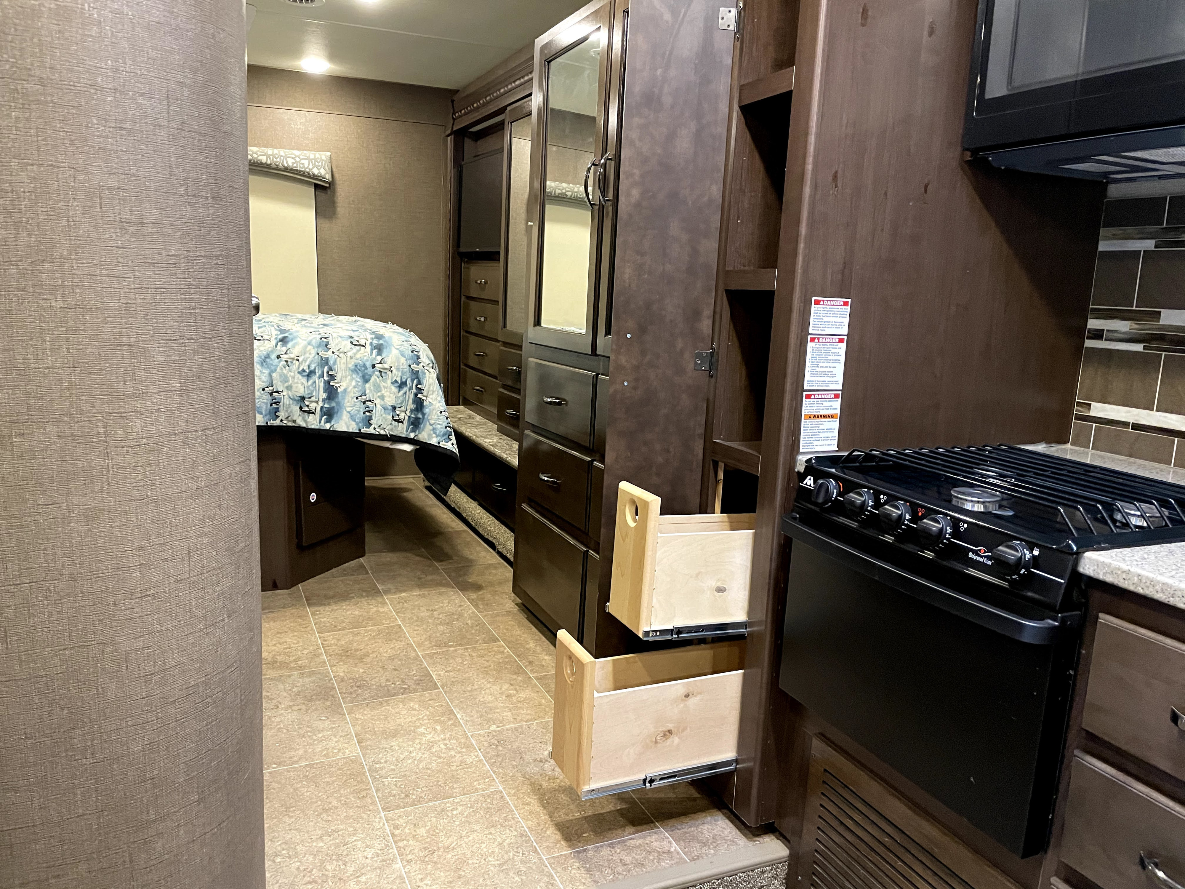 This RV rental showcases a cozy interior with a bed, wardrobe, and kitchen stove, featuring open drawers for ample storage.. Thor Motor Coach Chateau 2017