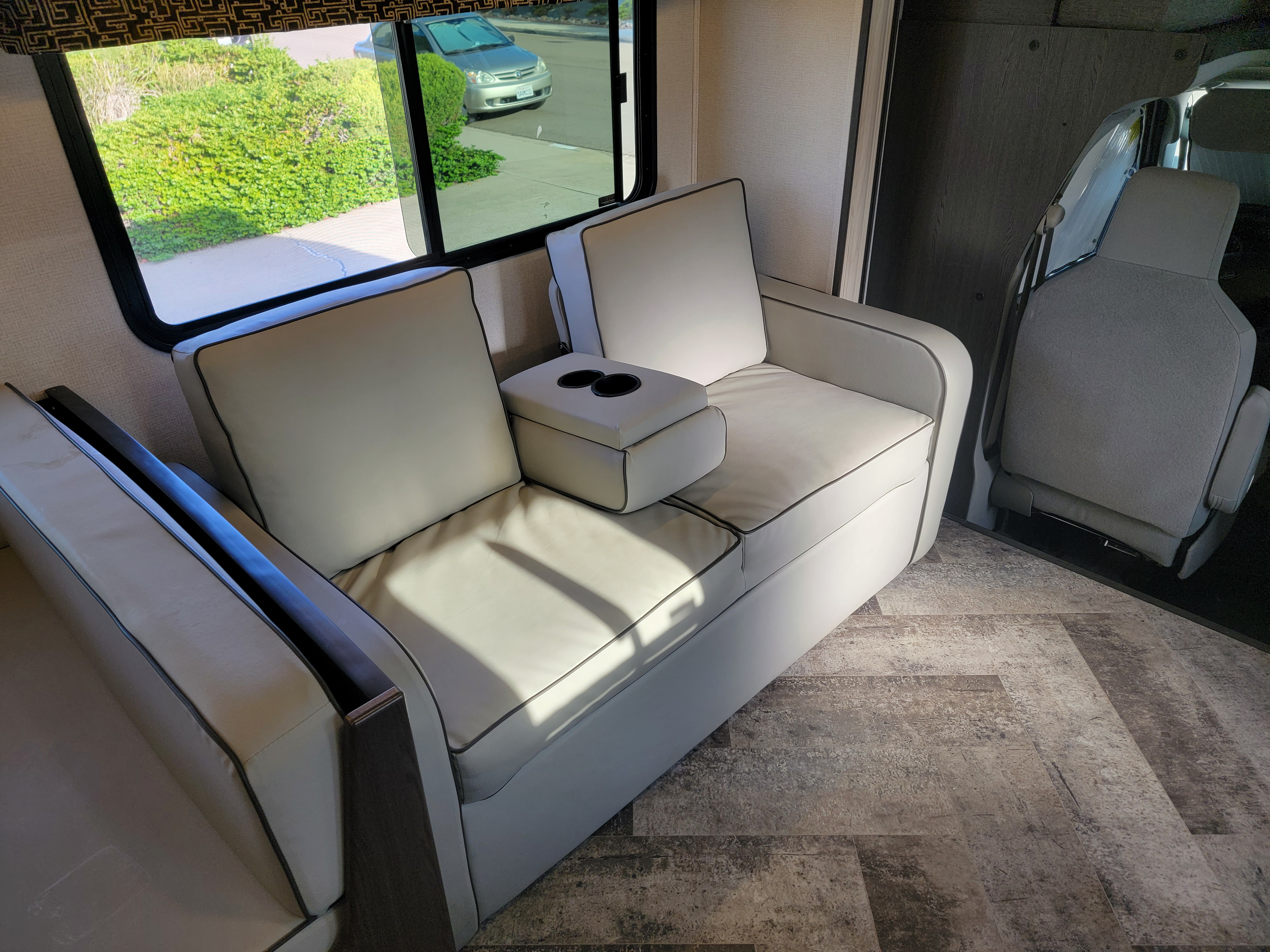 RV rental interior: light gray recliners with cup holders, a window revealing green bushes outside, and textured flooring.. Forest River Sunseeker 2021
