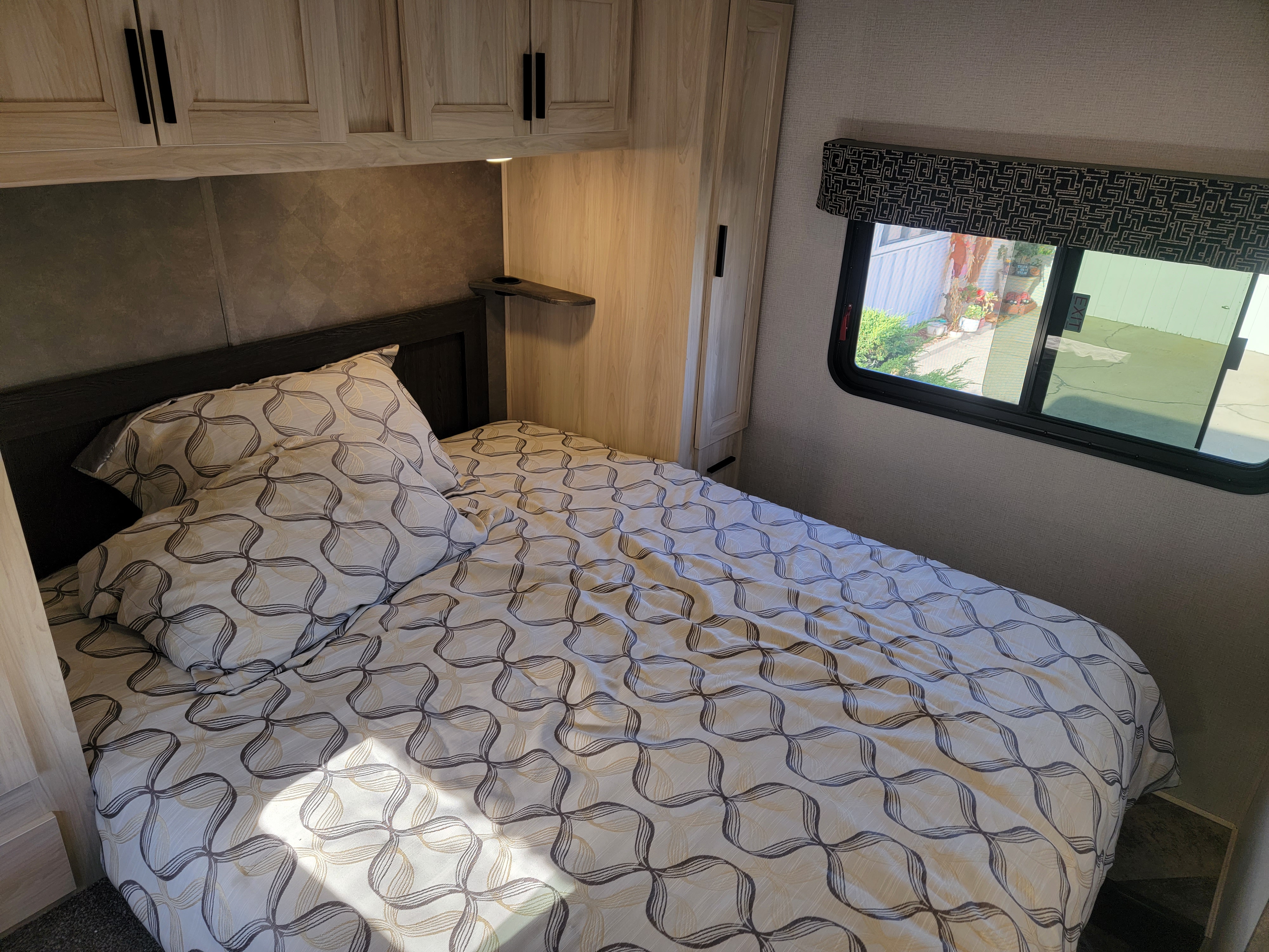 Comfortable RV rental bedroom with a bed featuring a geometric pattern, overhead storage, and a large window.. Forest River Sunseeker 2021
