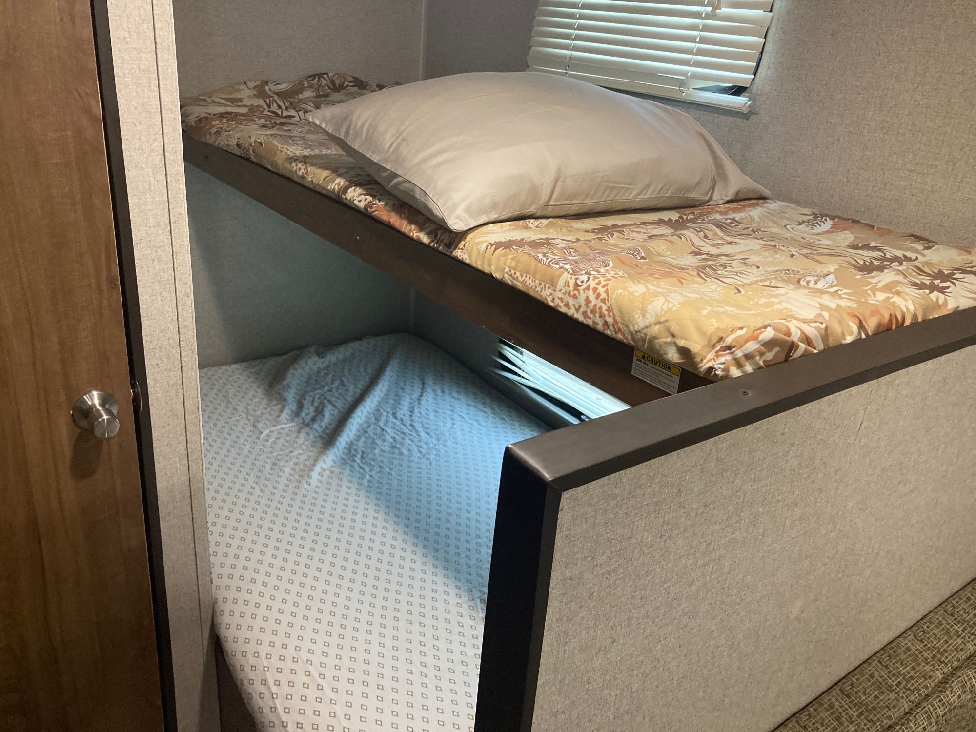 Comfortable bunk beds in an RV rental. The top bunk has a pillow and patterned sheet, the bottom bunk a subtle white sheet.. Dutchmen Aspen Trail 2018