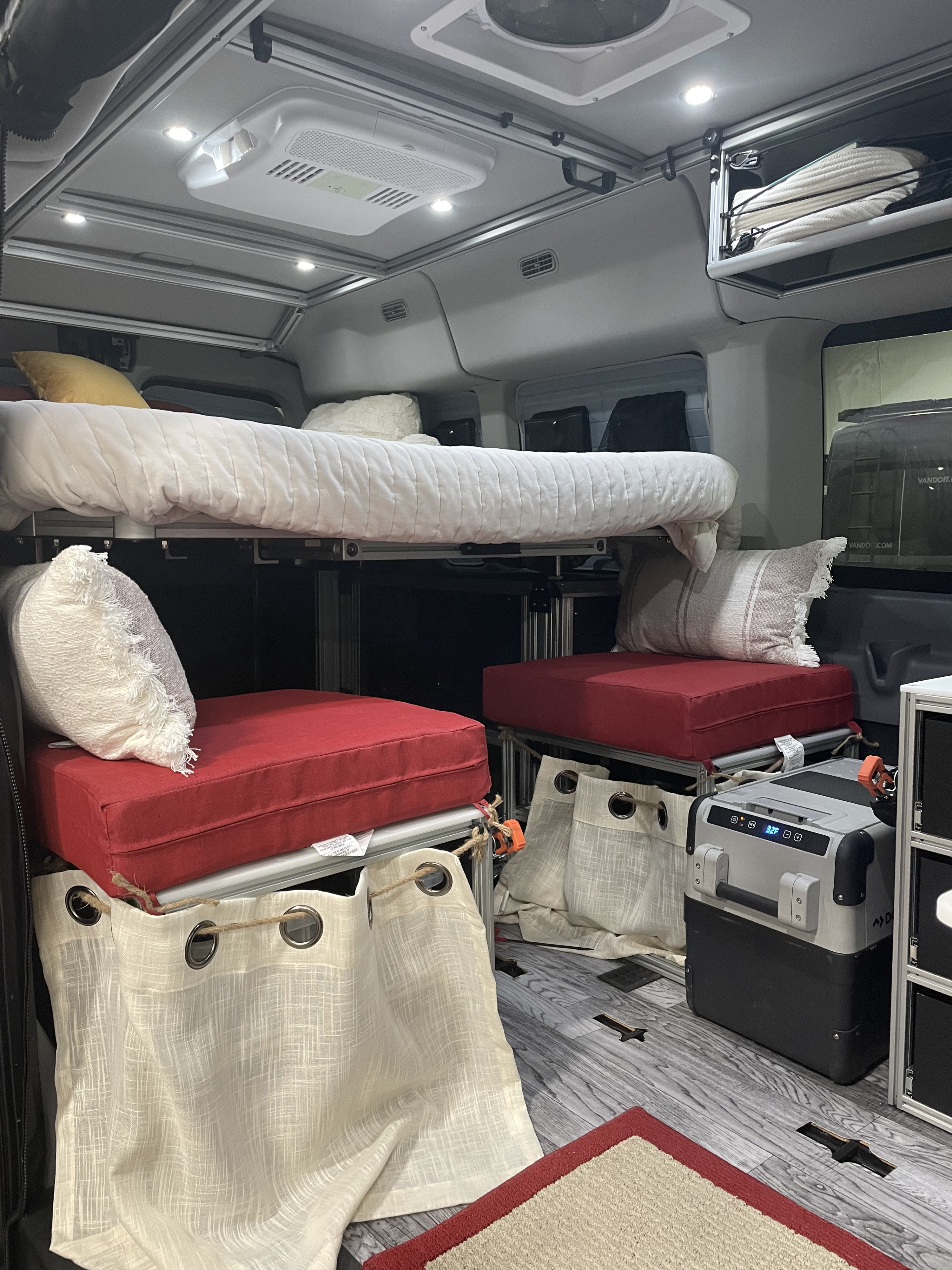 RV rental interior showcasing a bunk bed system, lower seating with red cushions, fridge, and overhead lighting.. Other Vandoit LIV 2019