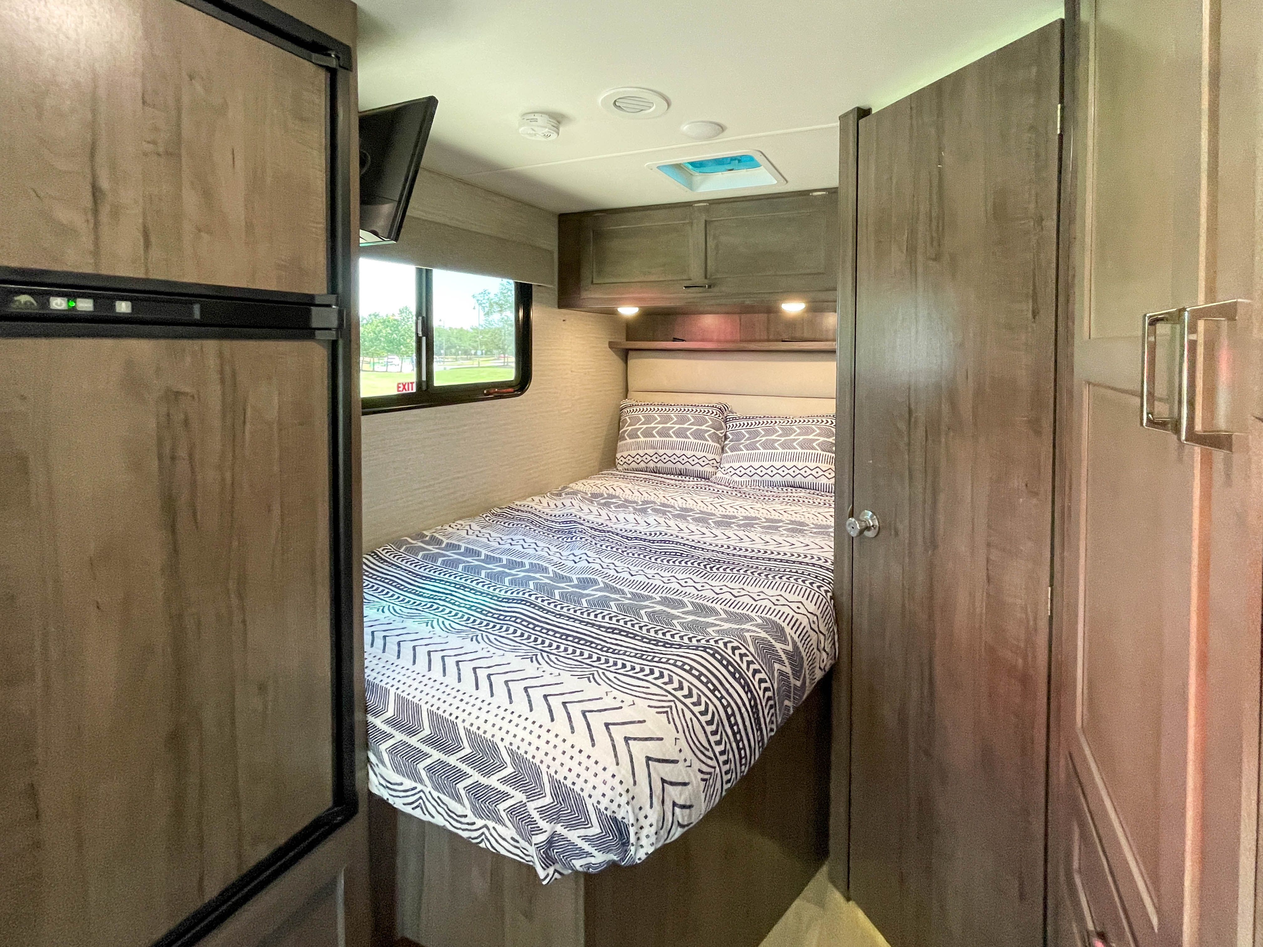 Cozy rv rental bedroom showing a bed with tribal print bedding, fridge, TV, & overhead cabinets. Compact comfort.. Winnebago Minnie Winnie 2020