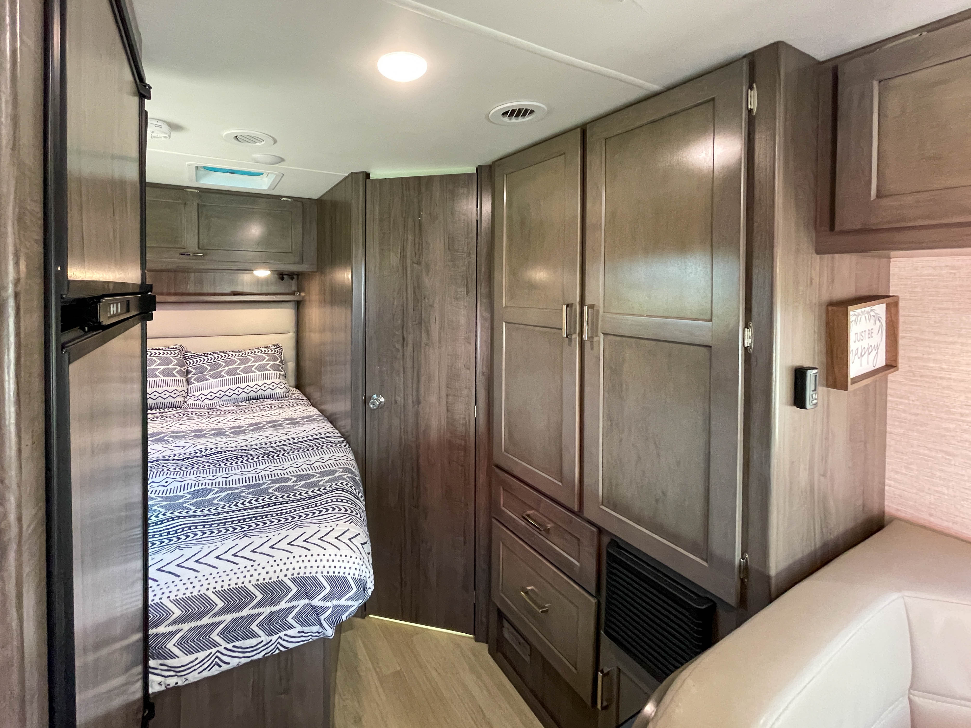 Inside this cozy RV rental: a comfortable bed with patterned bedding, built-in wood cabinets, and a glimpse of the living space.. Winnebago Minnie Winnie 2020