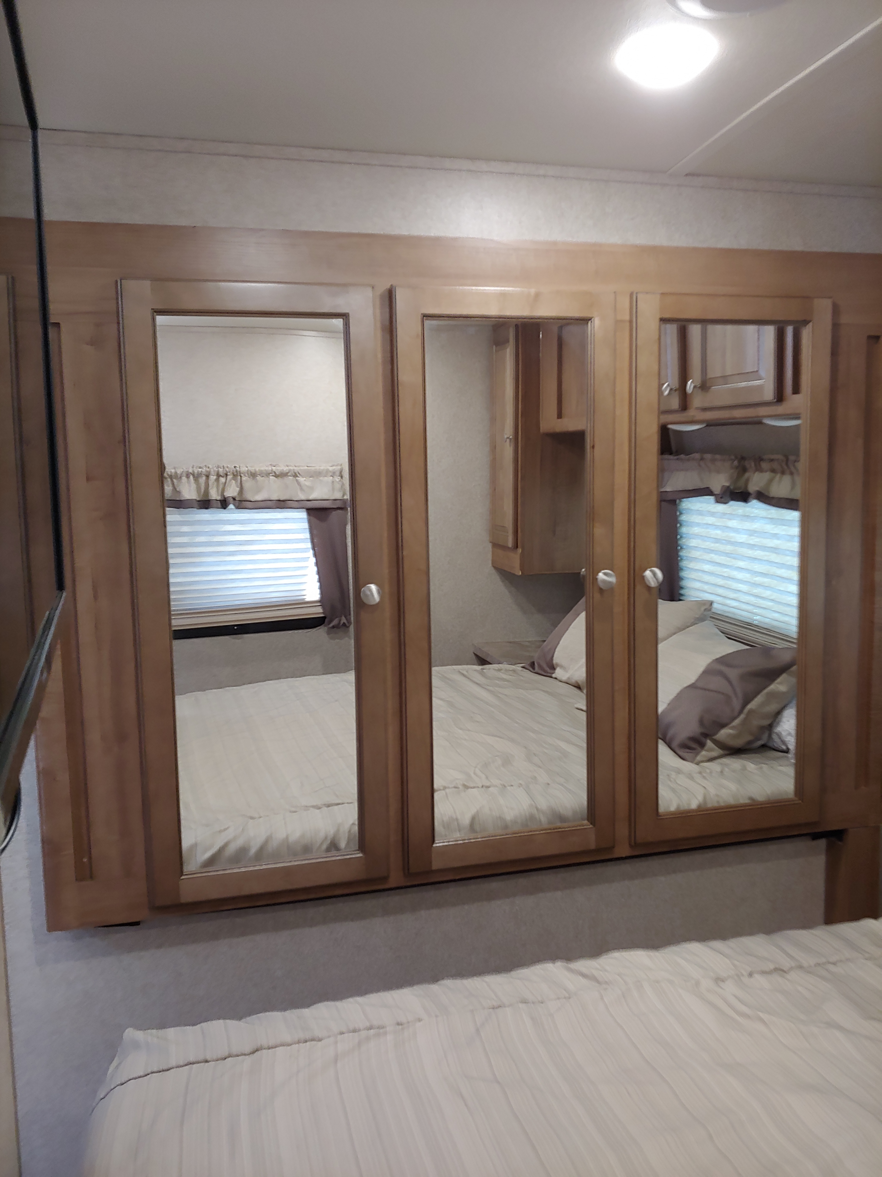 RV rental bedroom featuring mirrored wardrobe doors reflecting a comfortable bed and window with blinds.. Forest River Rockwood Signature Ultra Lite 2017