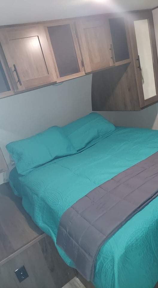 RV rental bedroom: a comfortable space with teal bed, overhead cabinets, and built-in mirrored storage.. Prime Time Avenger 2021