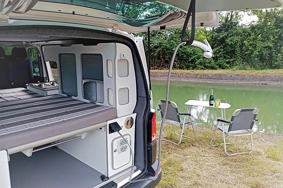 Scenic RV rental setup: camper van interior with bed & kitchen, plus an outdoor shower and riverside picnic area with chairs.. Volkswagen Transporter T6.1 2022